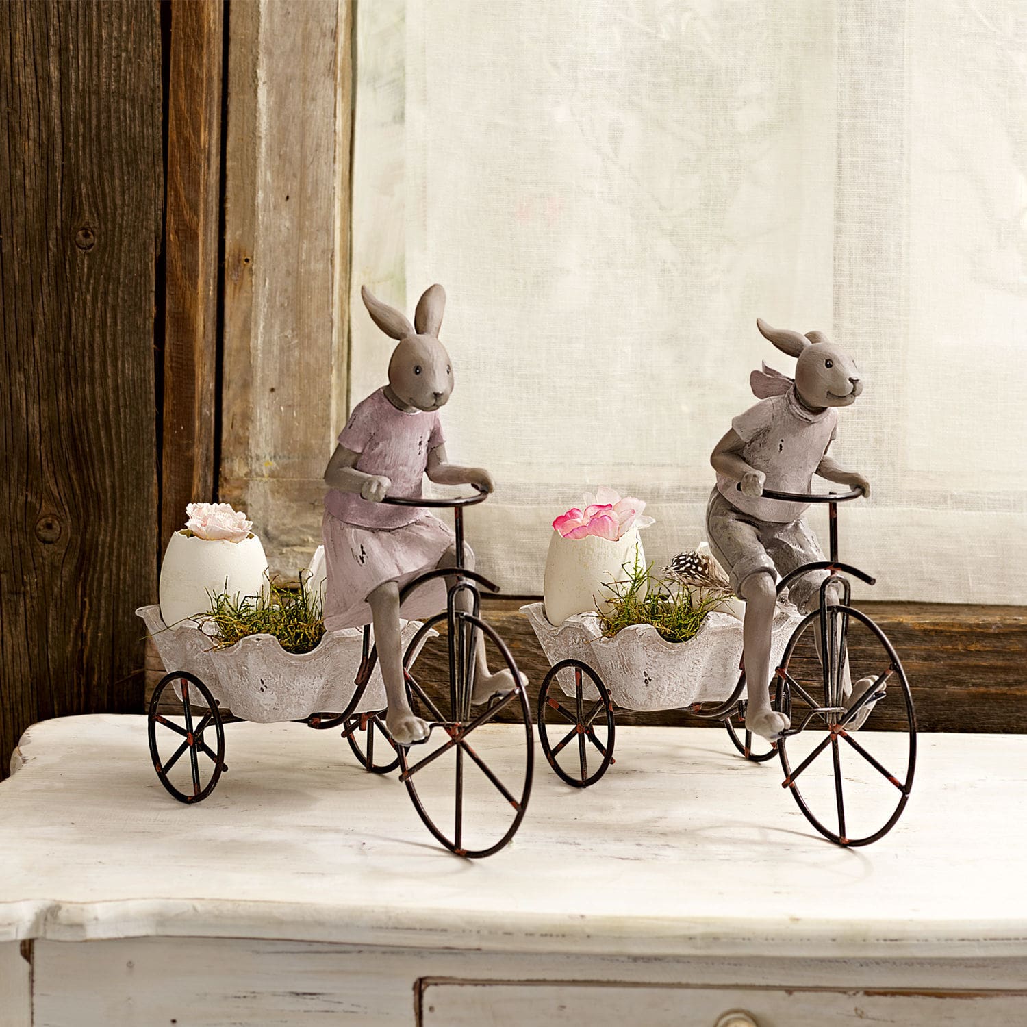 Decoratieve konijnenfiguren op metalen fietsen met witte bloempotten en bloemen op tafel