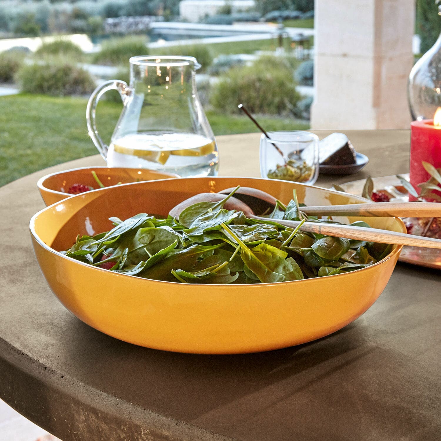 Coupe Calvi Saladier en céramique jaune avec couverts en bois sur une table extérieure