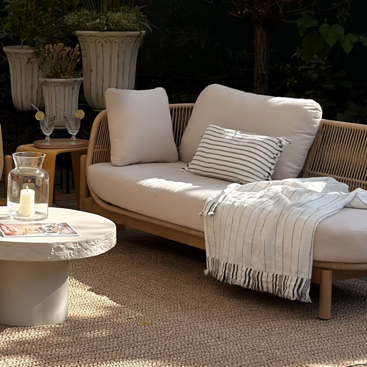 Moderne loungesofa met lichte kussens en gestreept plaid op natuurlijke buitenmat in tuin