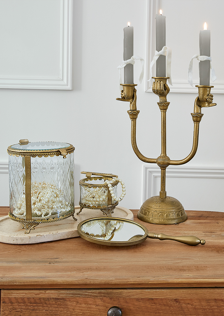 Chandelier doré à trois branches avec bougies et boîtes en verre contenant des perles sur table en bois