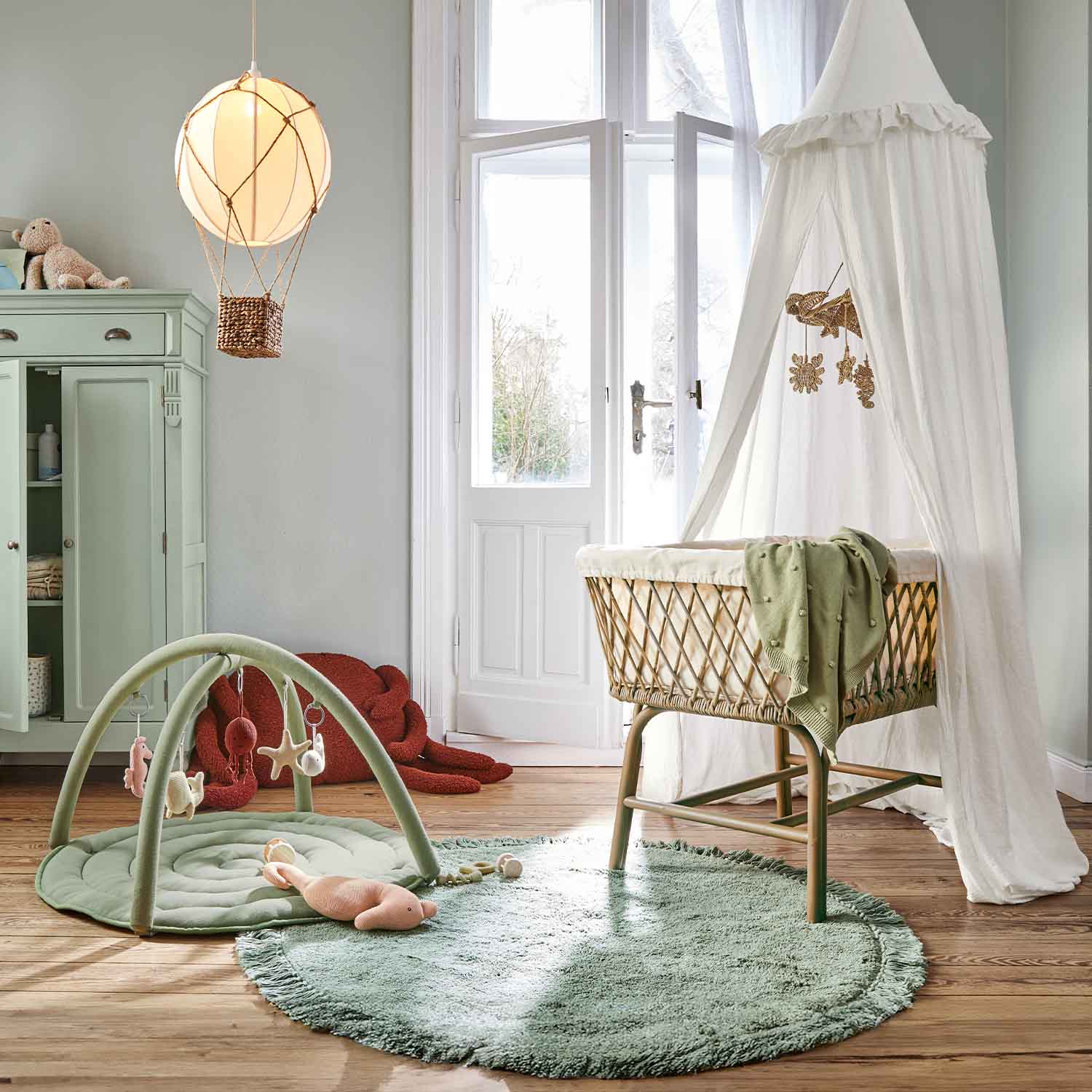 Chambre d'enfant avec berceau en osier et ciel de lit blanc, tapis vert et aire de jeu douce