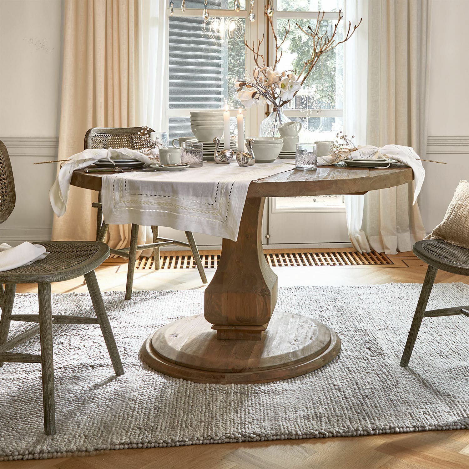 Tafel Alderwick Ronde houten tafel met wit tafelkleed en decoratie in lichte, gezellige eetkamer met natuurlijk licht