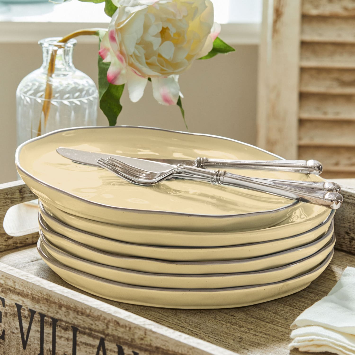 Ensemble d'assiettes en céramique crème avec bord métallique et couverts argentés sur plateau en bois