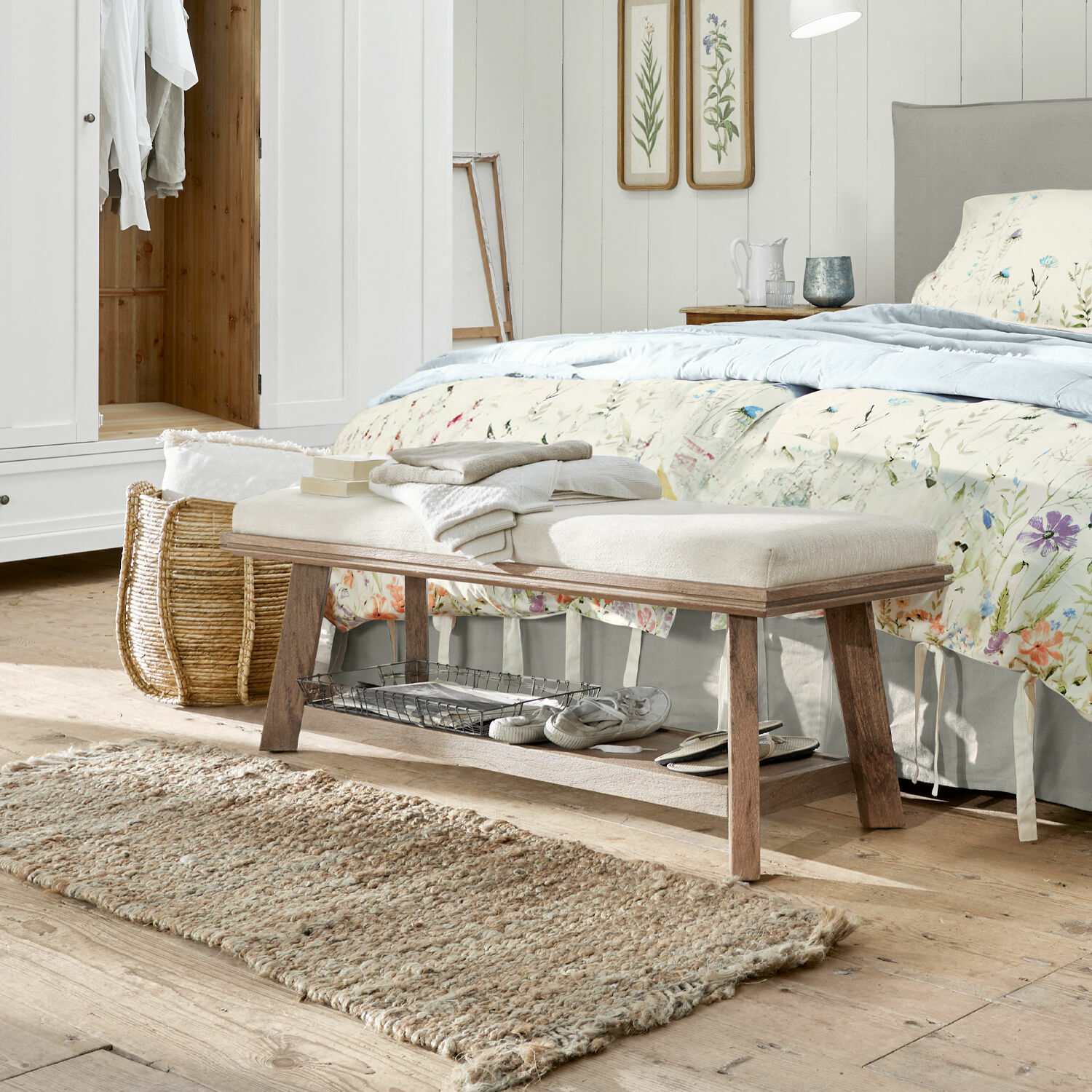 Houten bankje met licht gestoffeerde zitting in slaapkamer, natuurlijke vloerkleed en bloemendecoratie