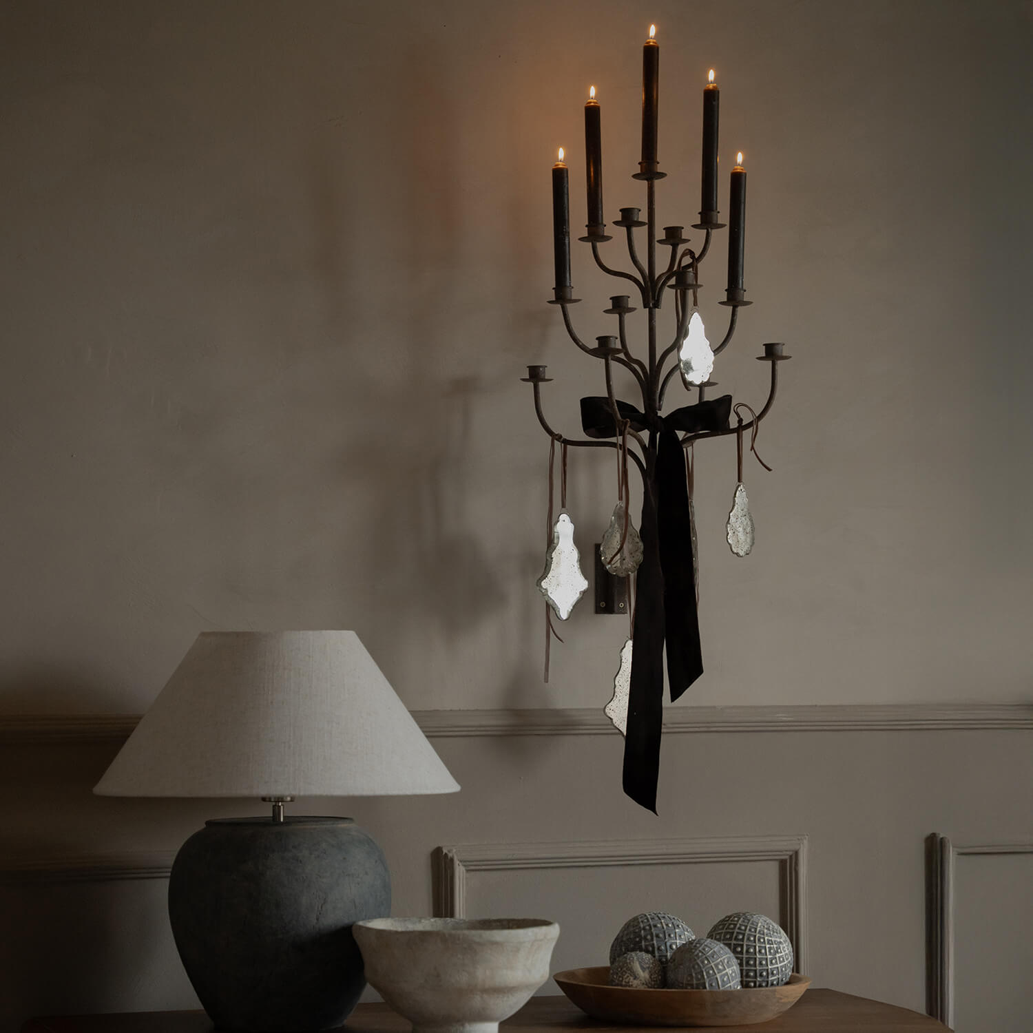 Applique murale en métal avec bougies noires et décorations vintage sur mur beige dans un intérieur cosy