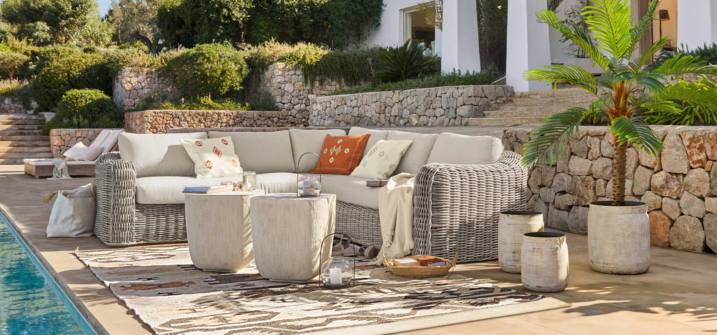 Tuinmeubelset van grijs rattan met crèmekleurige kussens en decoratieve kussens bij het zwembad