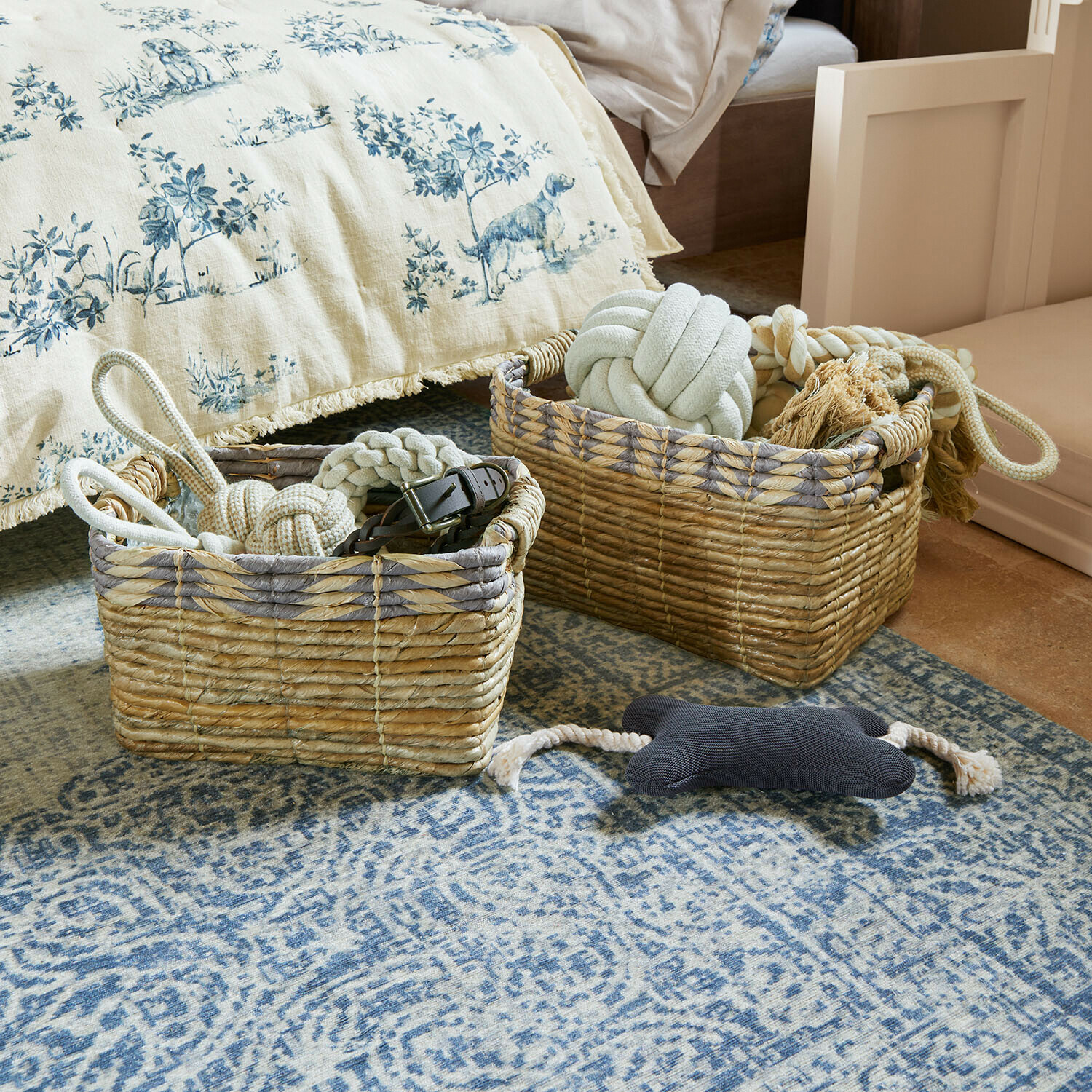 Lot de 2 paniers Kalimonde Deux paniers en osier naturel avec jouets pour chiens sur un tapis bleu dans une chambre à coucher