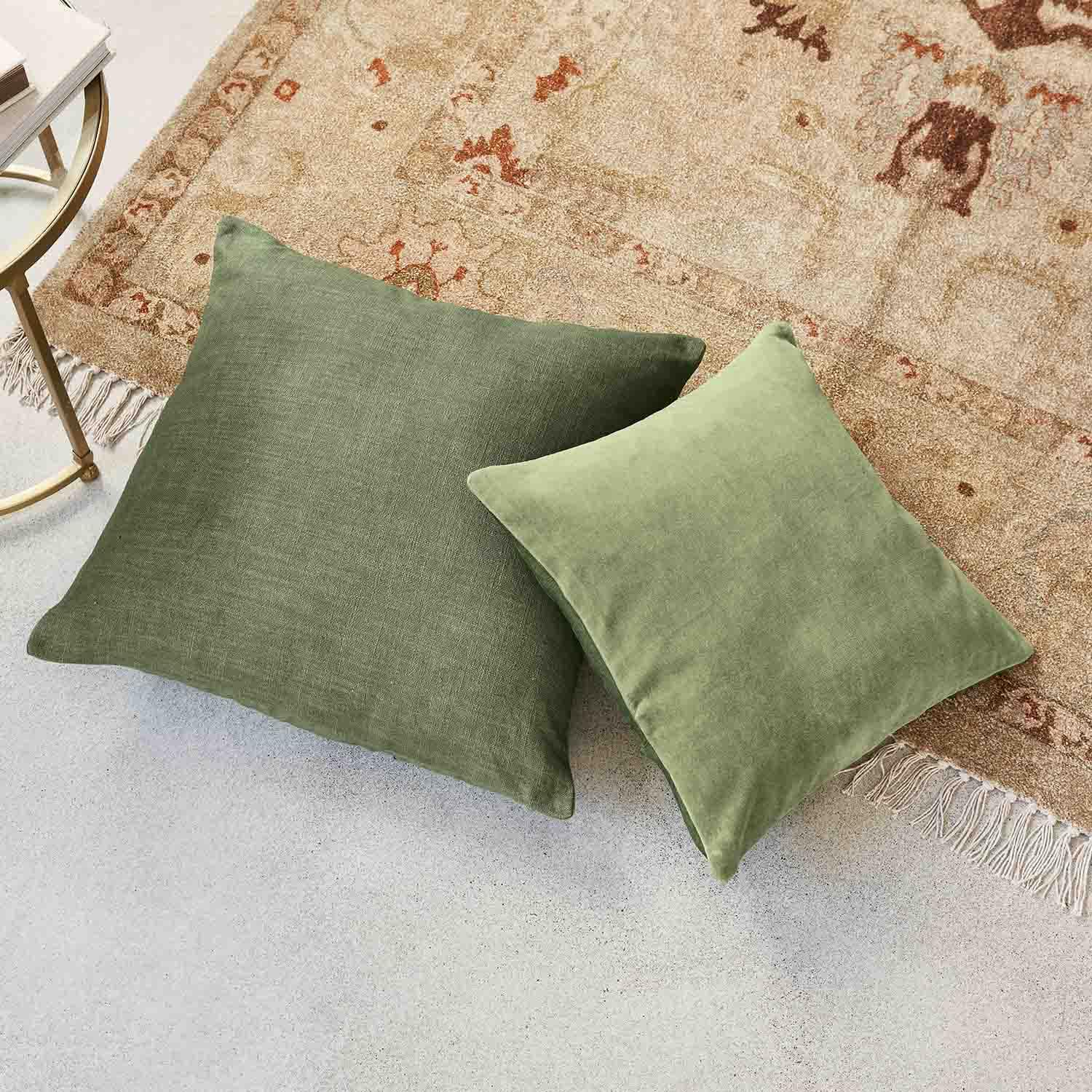 Deux coussins verts en tissu posés sur un tapis beige à franges, accessoires déco pour salon moderne
