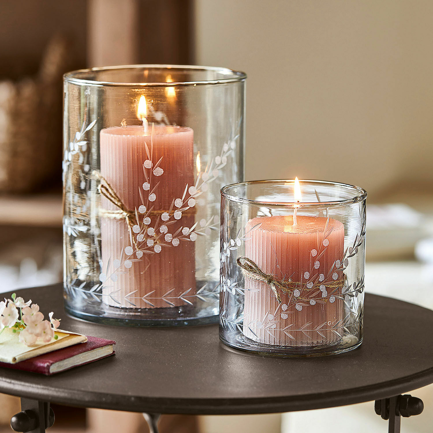Windlicht set van 2 Temao Twee roze kaarsen in transparante glazen windlichten met wit plantenpatroon op een tafel