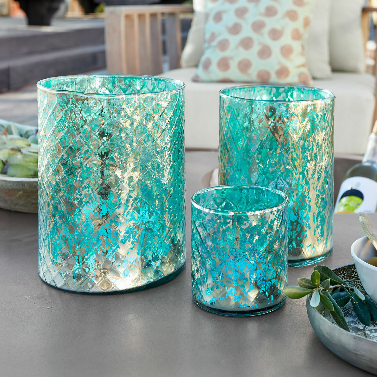 Windlichtje set van 3 Firalen Set van drie turquoise glazen windlichten met metalen patroon op tuintafel