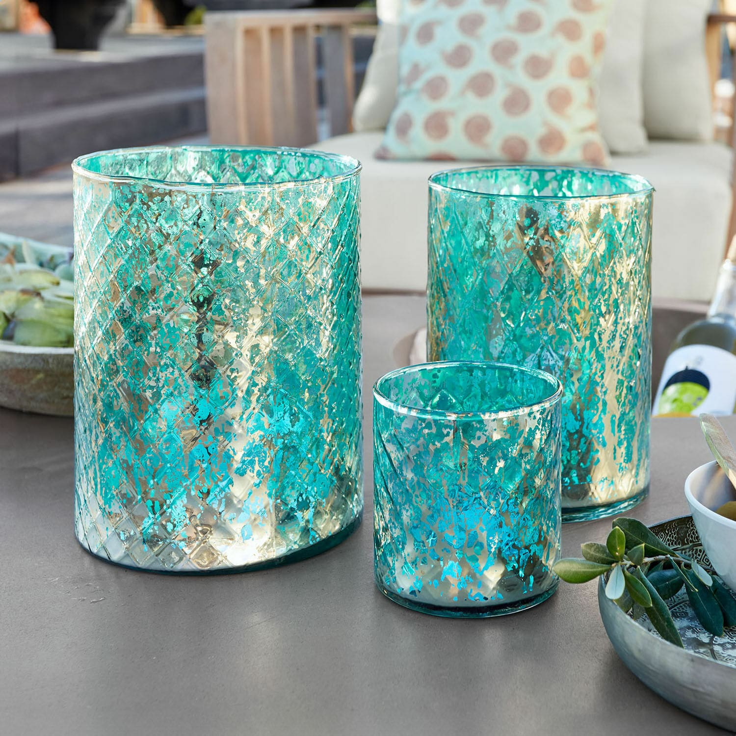 Lot de 3 photophores Firalen Ensemble de trois photophores en verre turquoise avec motif métallique sur une table extérieure