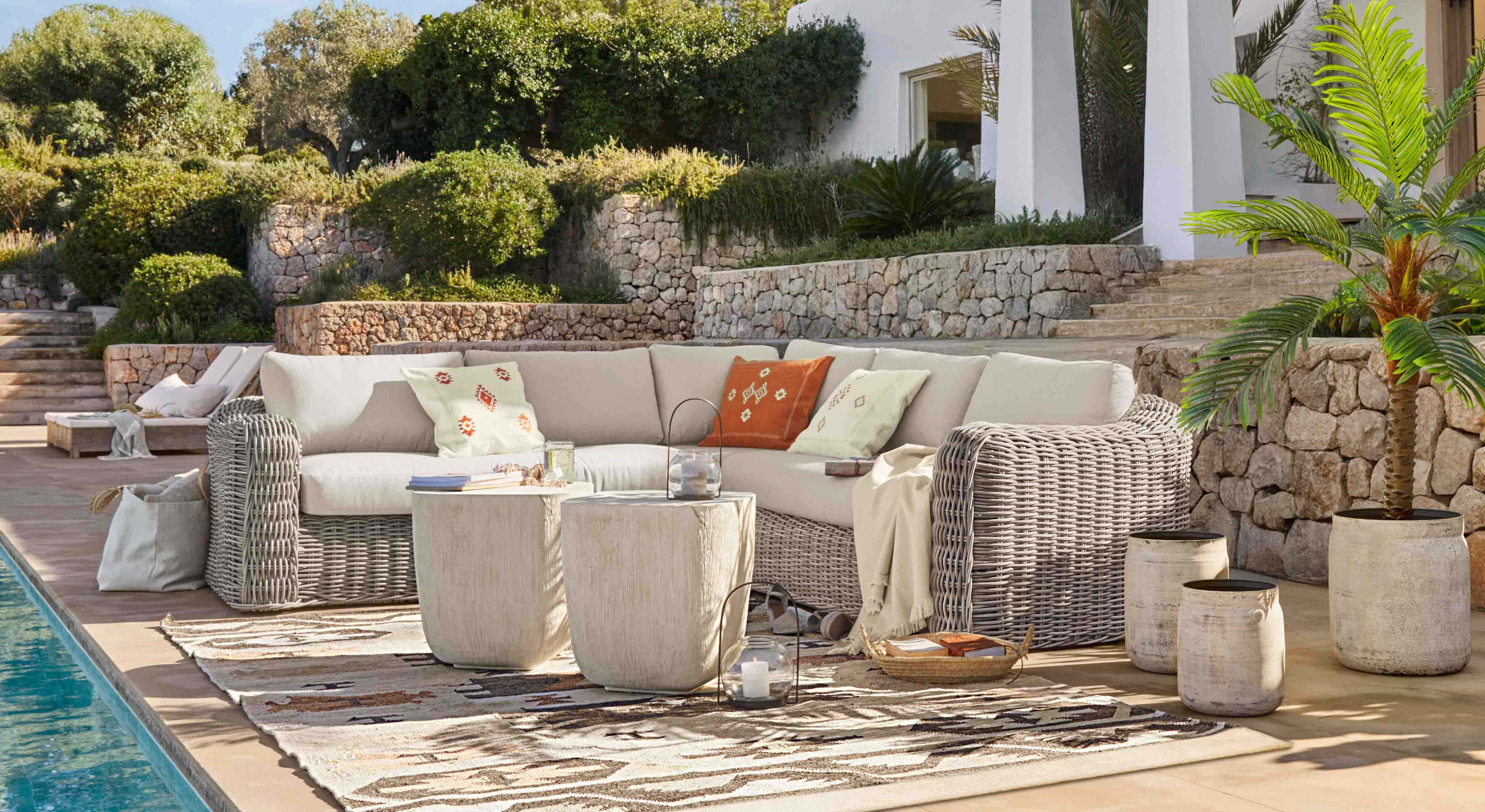 Tuinmeubelset van lichtgrijs rattan met crèmekleurige kussens en decoratieve kussens op terras bij zwembad