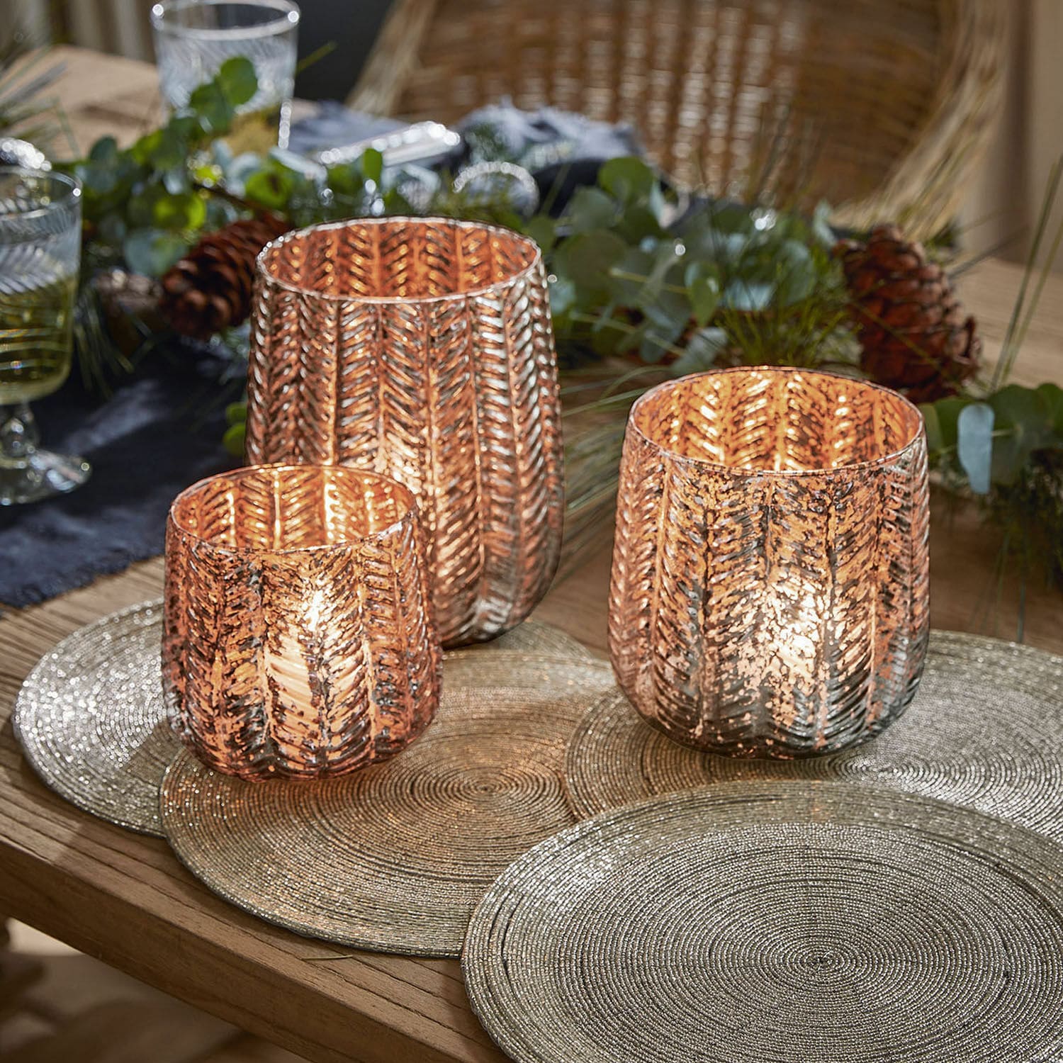 Ensemble de trois photophores en verre cuivré avec motif feuille sur table en bois décorée pour les fêtes