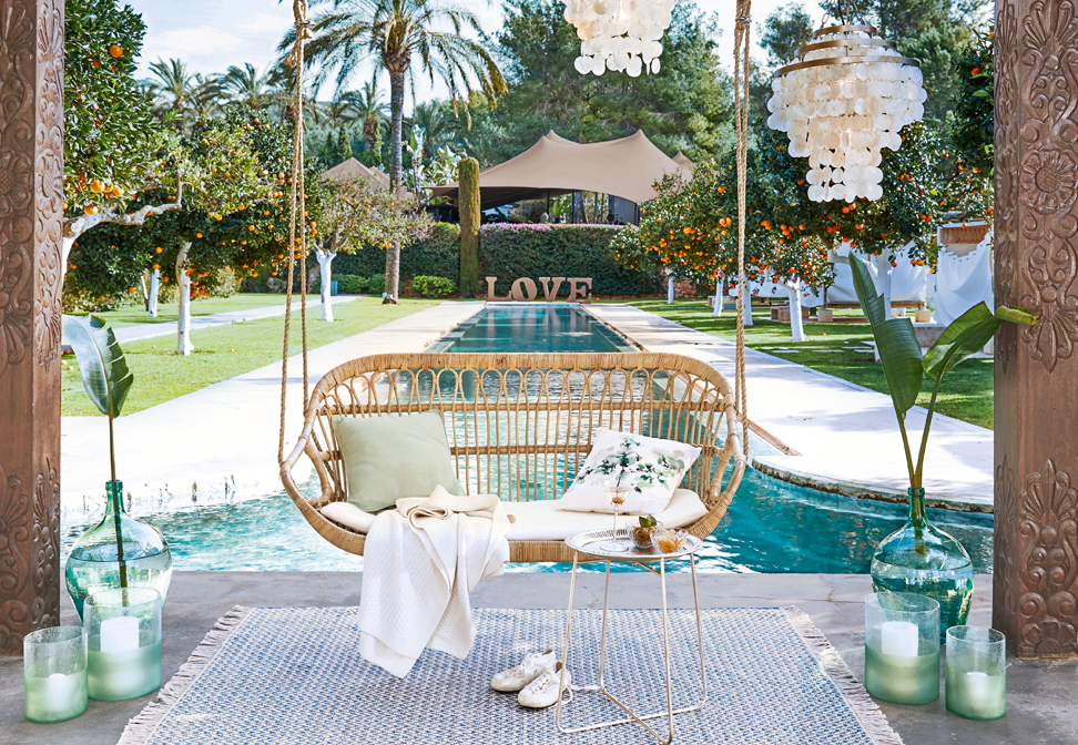 Balançoire en rotin avec coussins au-dessus d'une piscine dans un jardin avec des orangers et décorations
