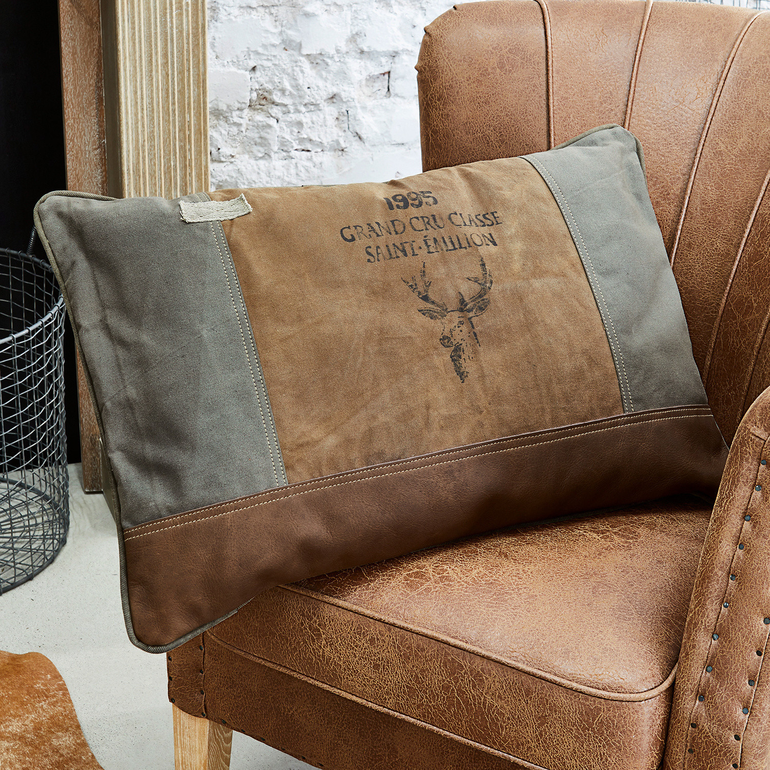 Kussen Chiron Bruin-grijs sierkussen met hertenprint op een bruine leren stoel in vintage stijl