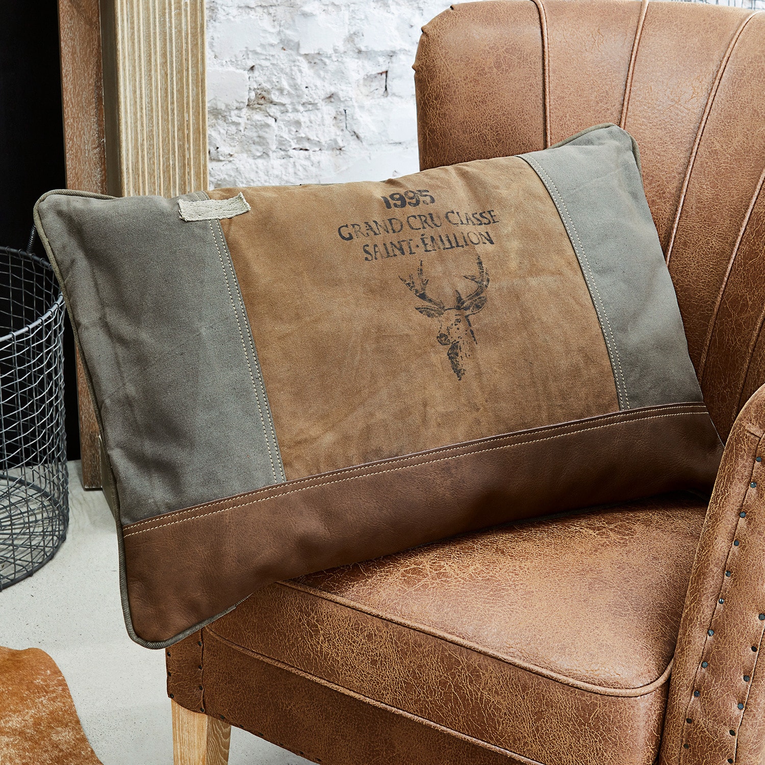 Kussen Chiron Bruin-grijs sierkussen met hertenprint op een bruine leren stoel in vintage stijl