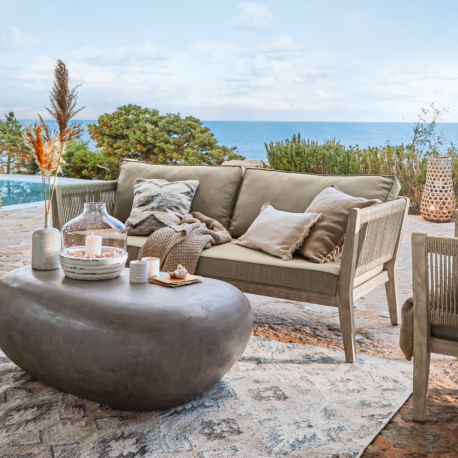 Canapé Biarritz Canapé d'extérieur beige en bois et tissu sur terrasse avec vue mer, table basse moderne en pierre