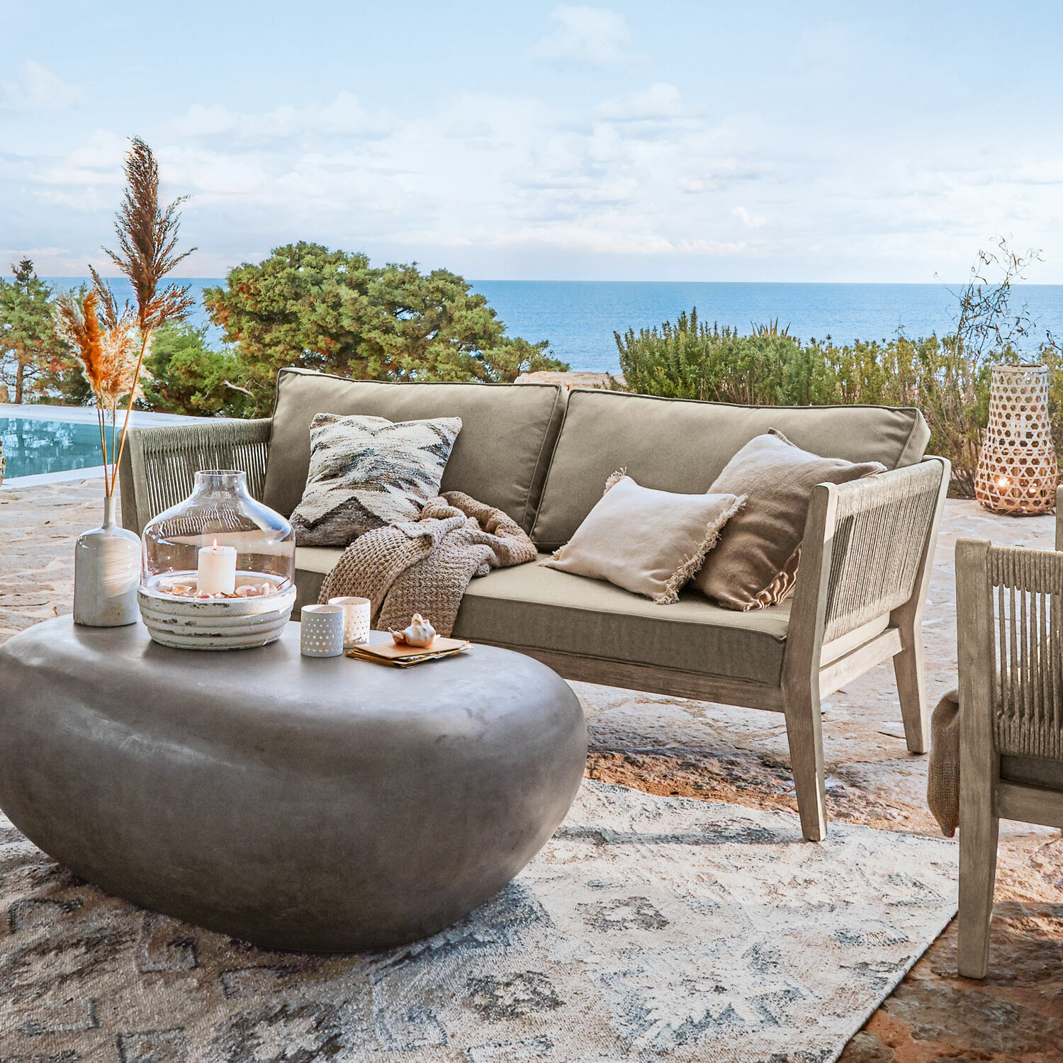 Bank Biarritz Beige buitenbank van hout en stof op terras met zeezicht, moderne stenen salontafel