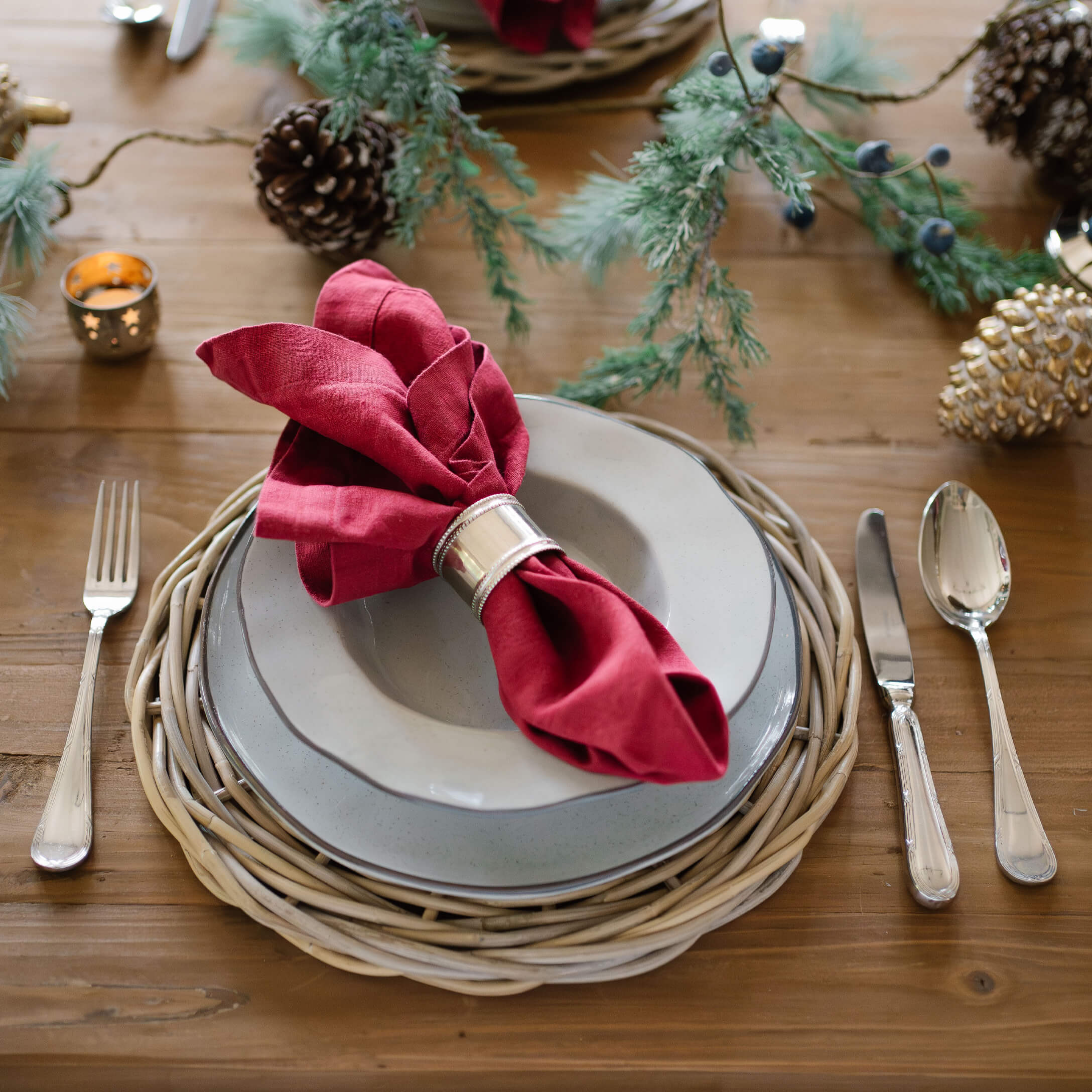 Service de table élégant avec assiettes grises, serviette rouge en lin et dessous de plat en osier naturel