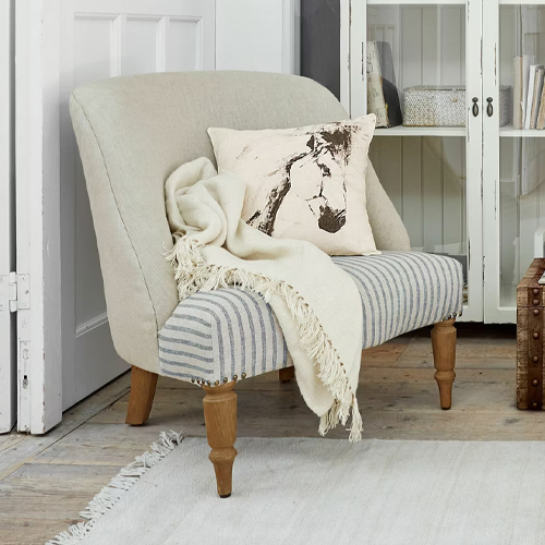 Canapé bicolore en tissu rayé et dossier beige avec pieds en bois, décoré d’un coussin et d’un plaid