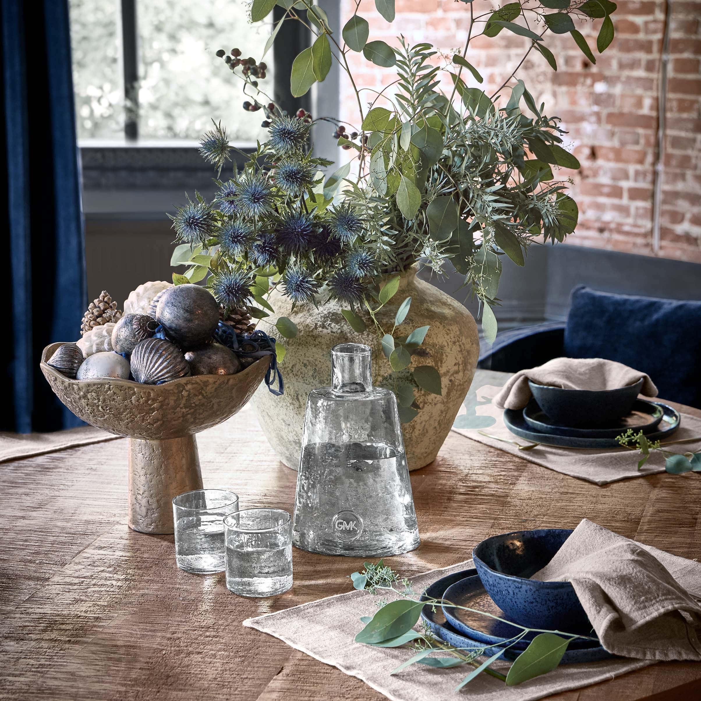 Decoratieve metalen schaal met sierobjecten en vaas met groene bladeren op houten tafel in woonkamer
