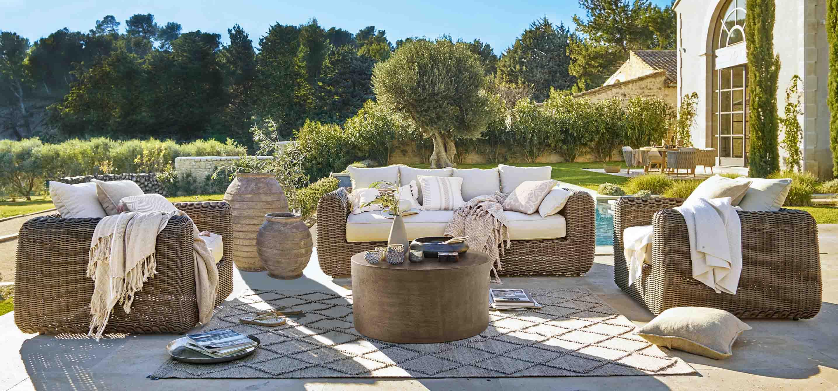 Ensemble de mobilier de jardin en rotin brun avec coussins crème et table basse sur terrasse ensoleillée