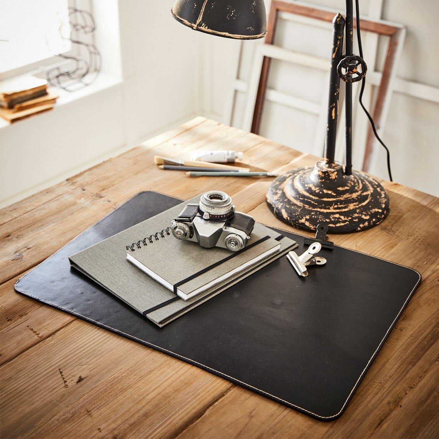 Bureaulegger Jansen Zwarte leren bureaulegger met notitieboekjes en vintage camera op lichte houten tafel