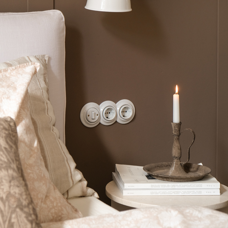 Rustieke metalen kandelaar met witte kaars op tafeltje naast bed met beige beddengoed