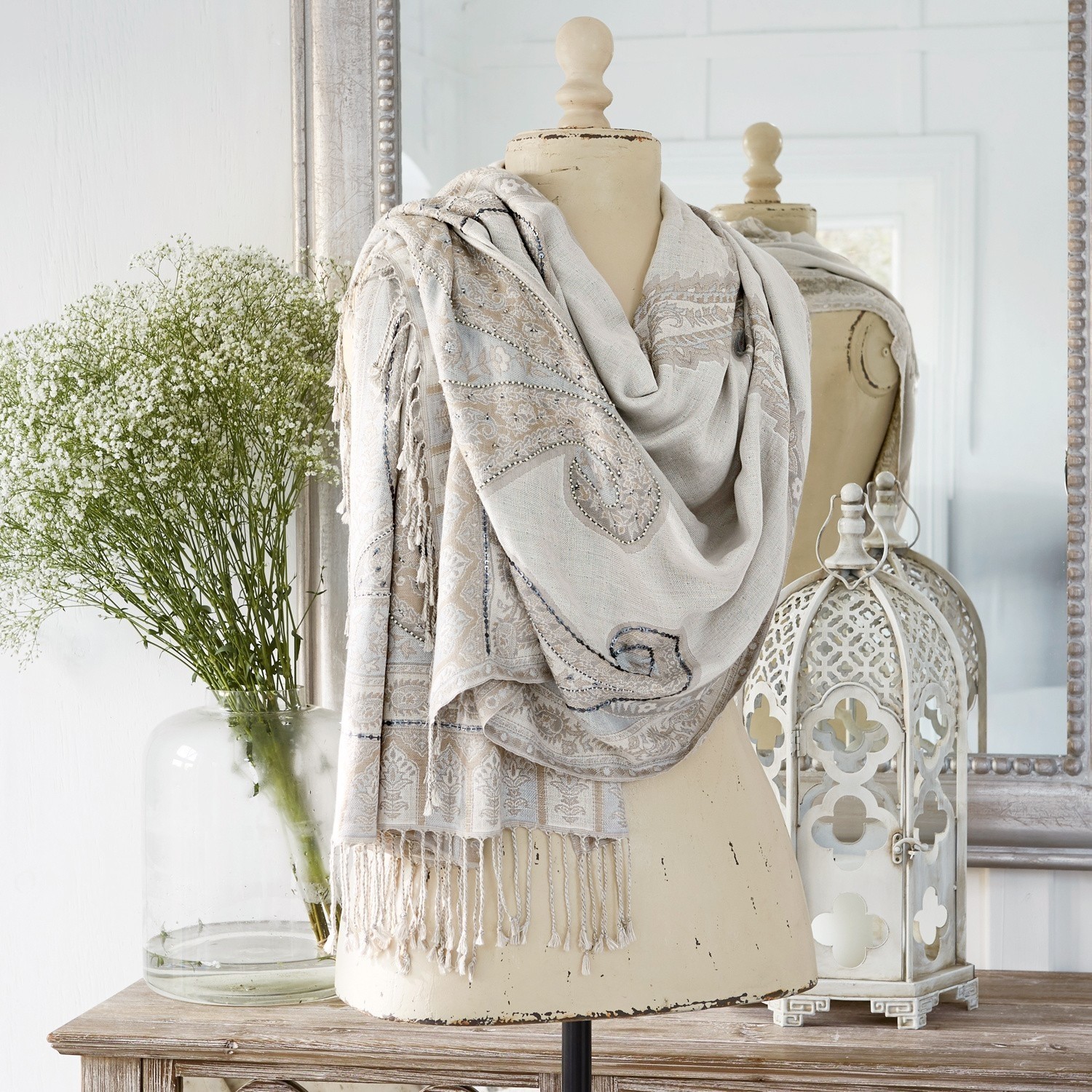Écharpe Moyra Écharpe beige à motif paisley avec franges sur mannequin, décor intérieur avec lanterne et fleurs