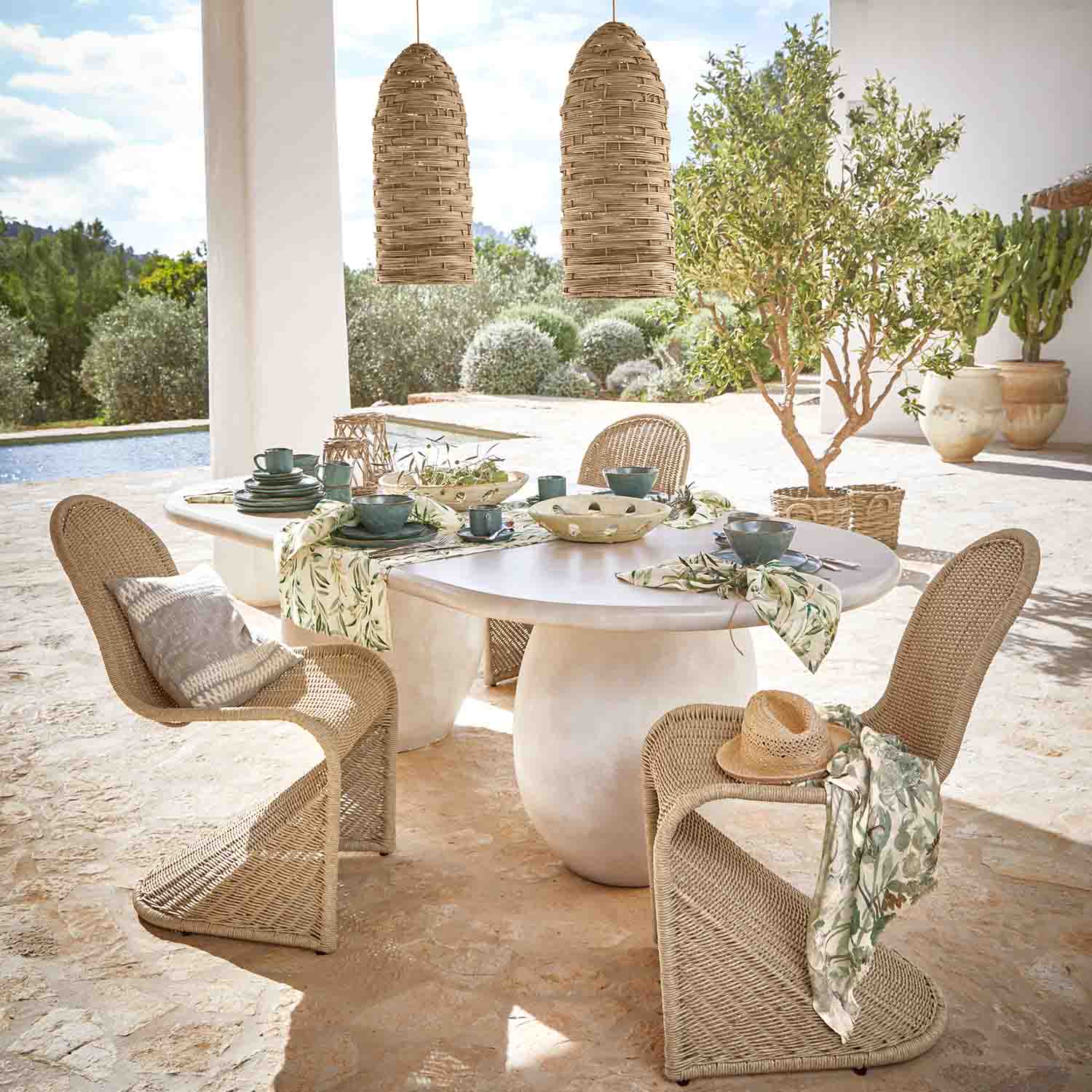 Ovale witte stenen tafel met rotan stoelen en natuurlijke hanglampen in zonnige tuin