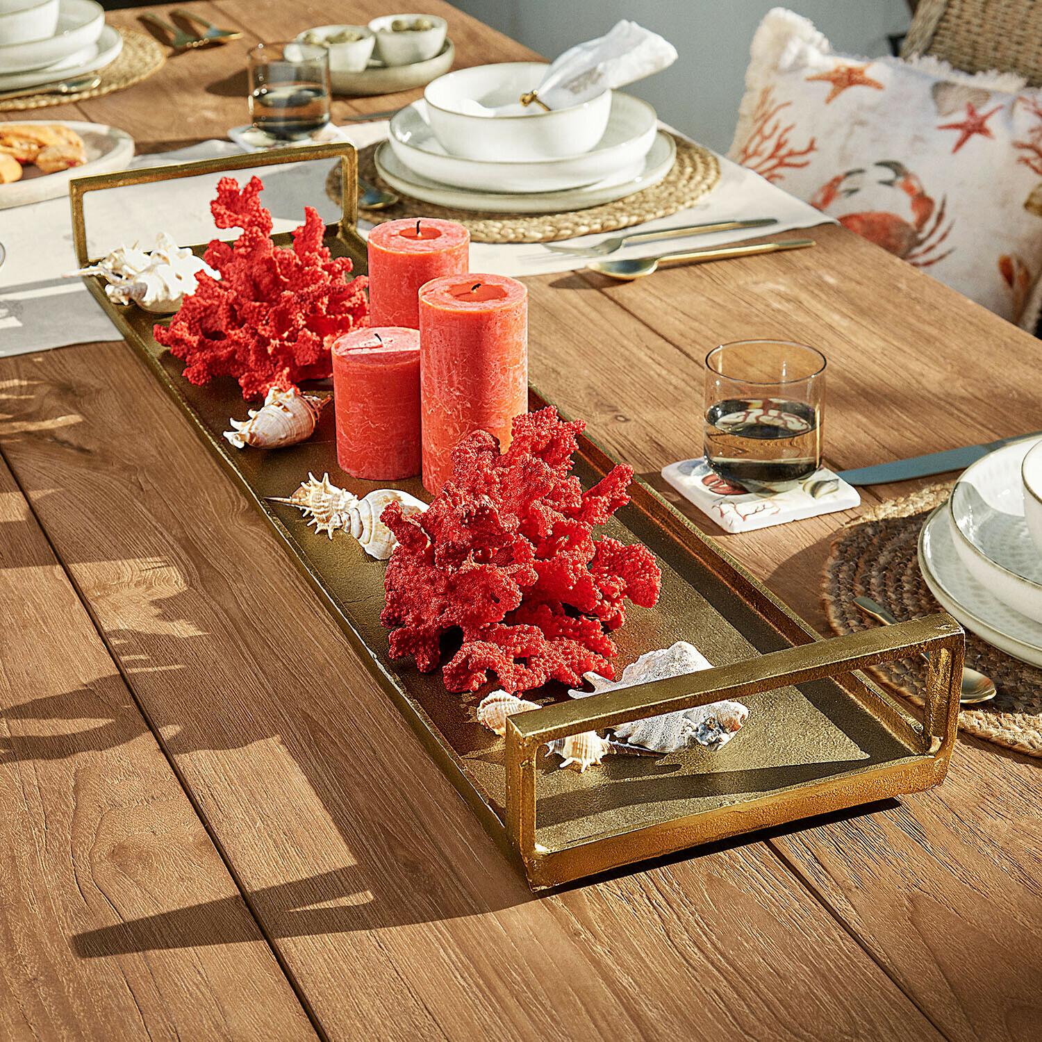 Plateau en métal doré avec bougies rouges et décorations corail sur table en bois
