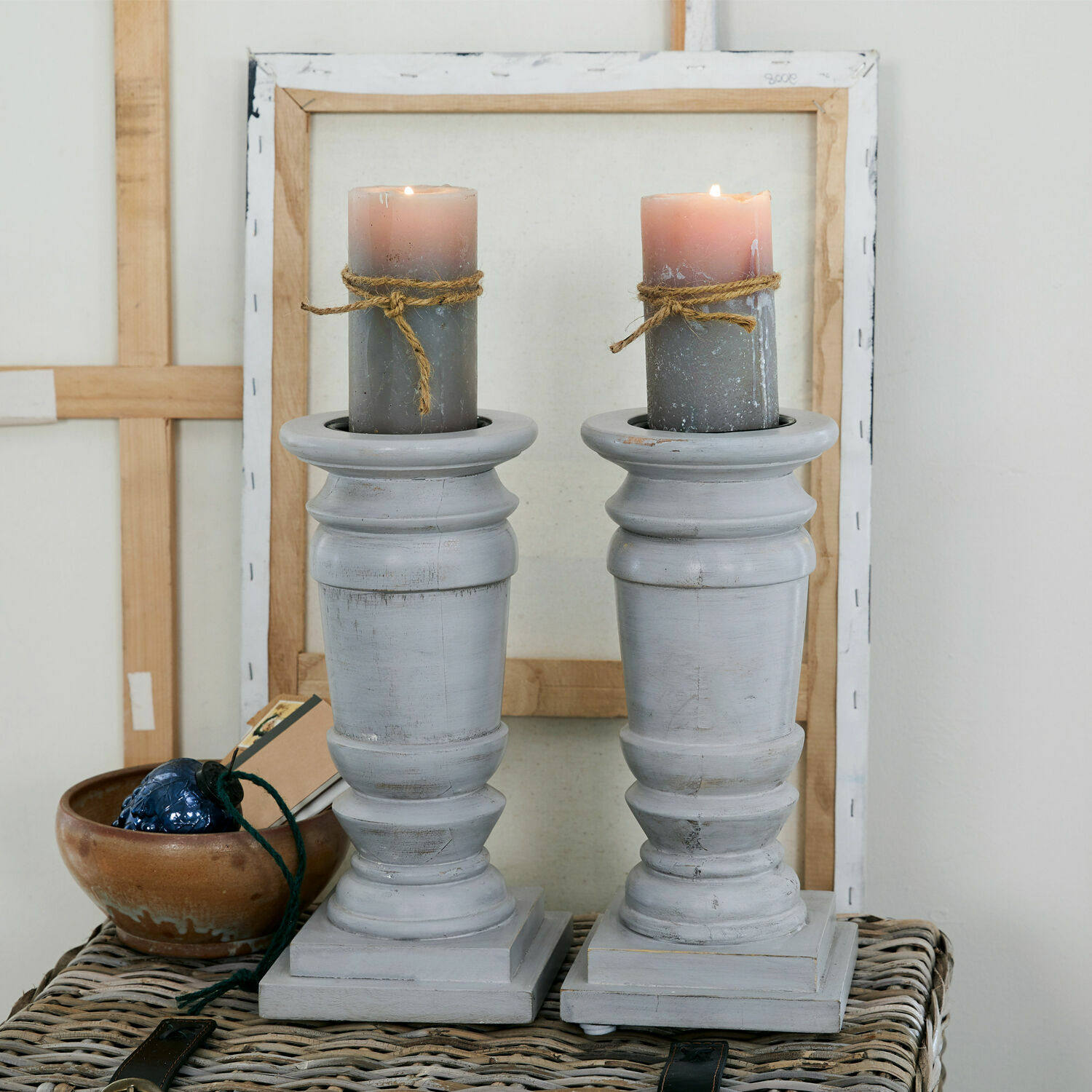 Kandelaar set van 2 Lobata Set van twee grijze houten kandelaren met grijze kaarsen en touwdecoratie op een rieten tafel