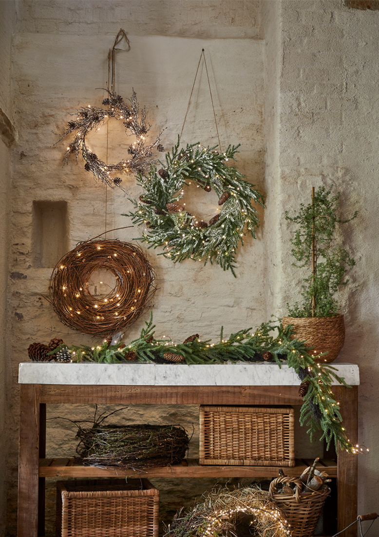Decoratieve kerstkransen van takken en lichtjes aan stenen muur en houten tafel met marmeren blad