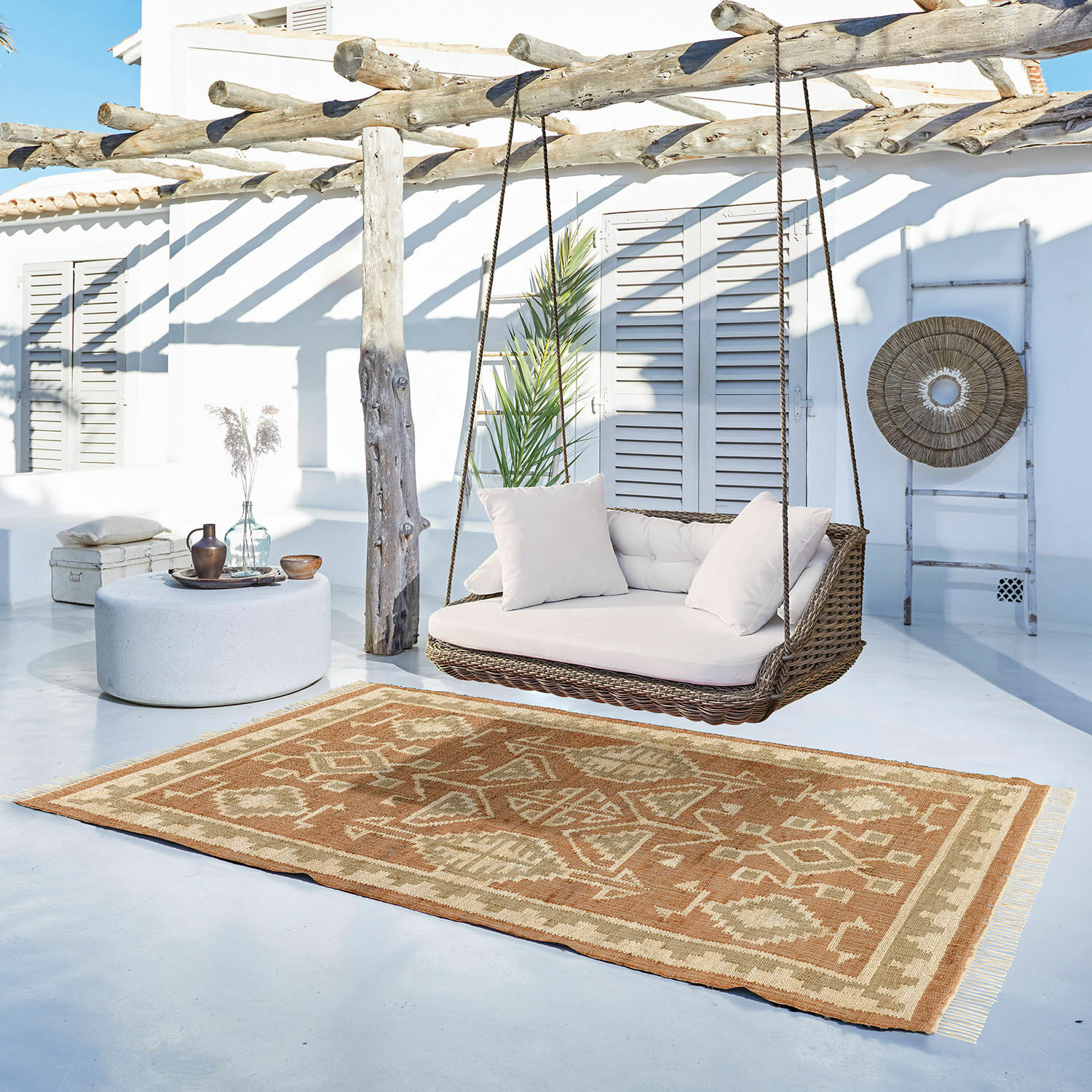 Vloerkleed Serenath Bruin-beige vloerkleed met geometrisch patroon op lichte veranda met rotan schommel en kussens