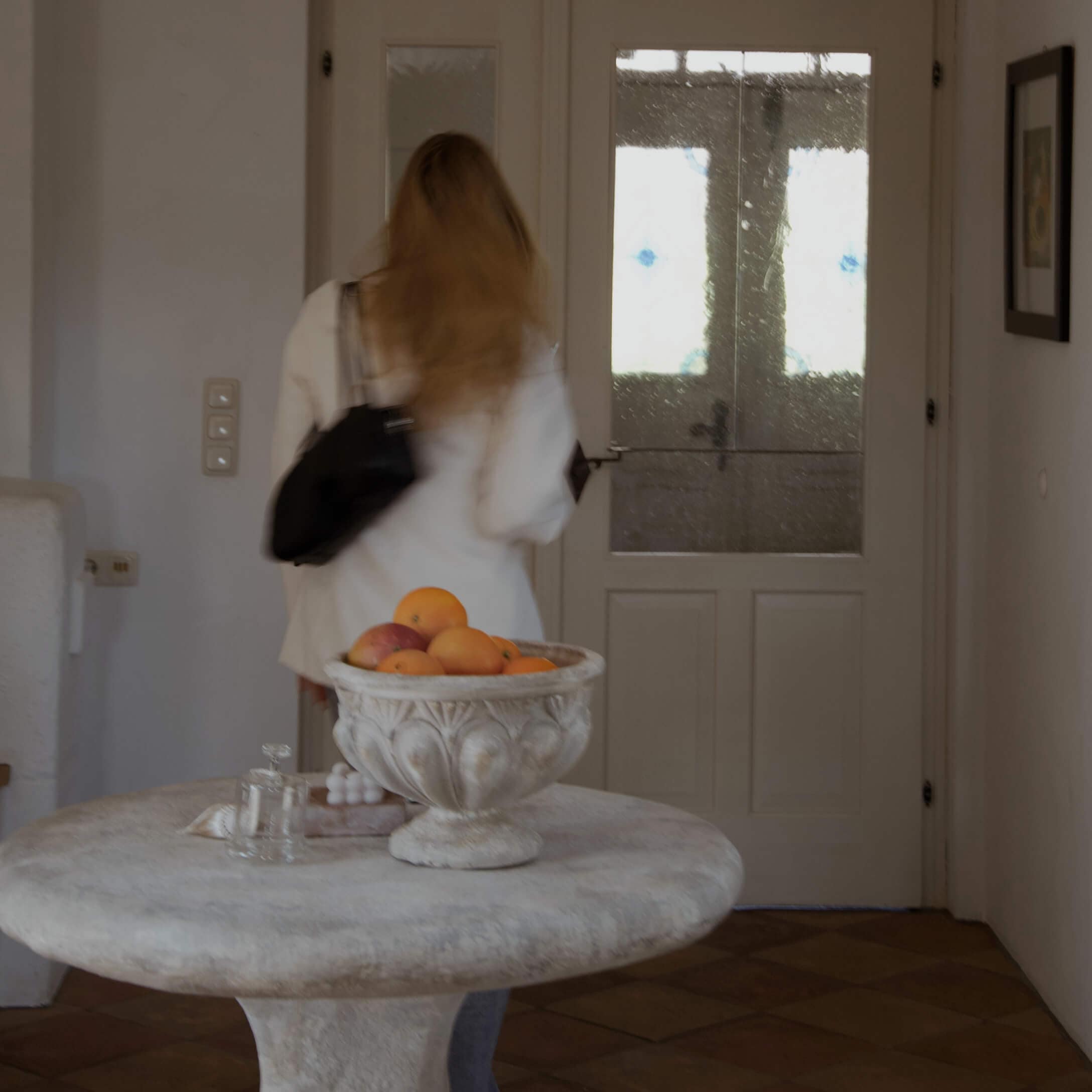 Coupe décorative en pierre avec des oranges sur une table ronde dans un intérieur lumineux avec porte vitrée.