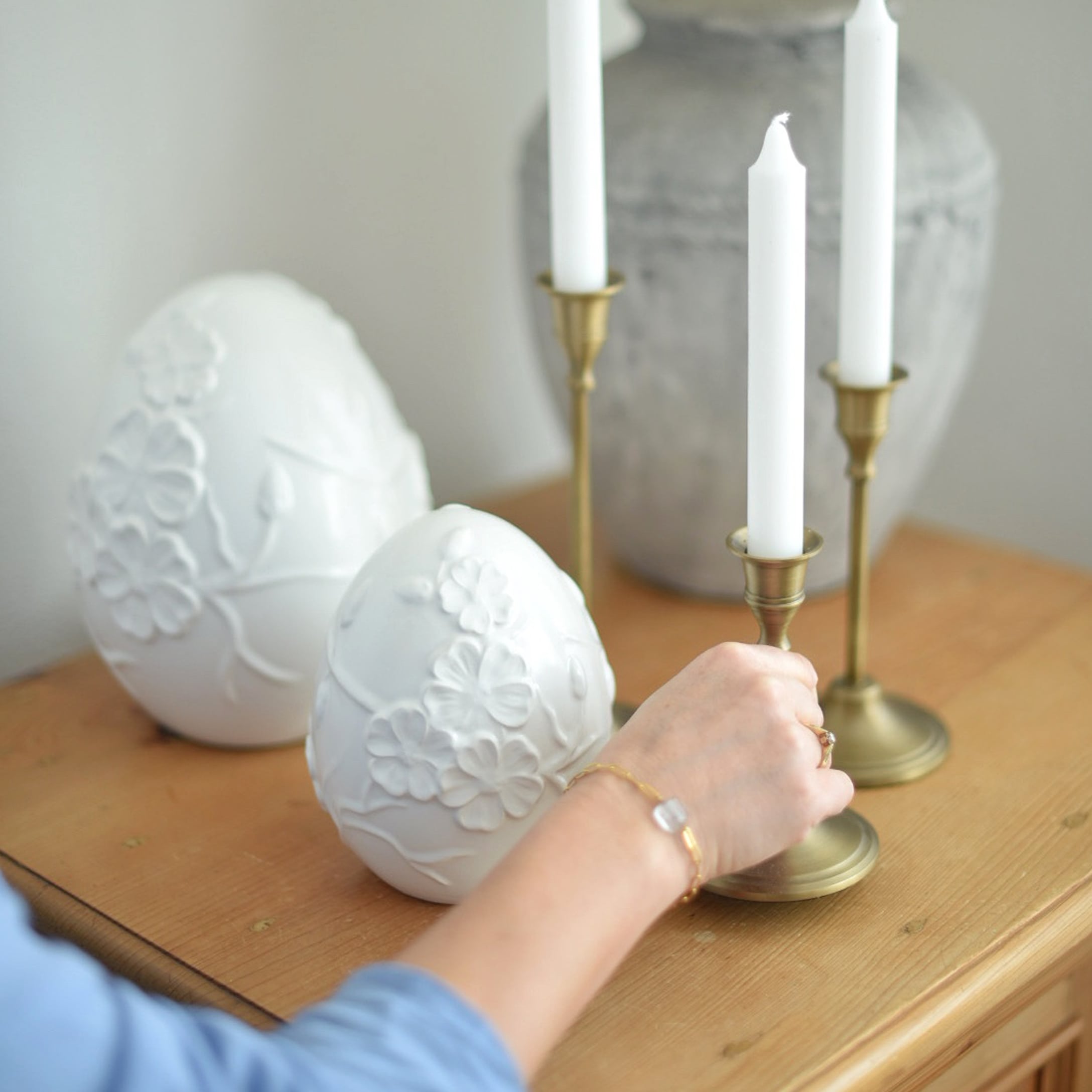 Witte keramische decoratieve eieren met bloemreliëf op houten tafel naast messing kandelaars