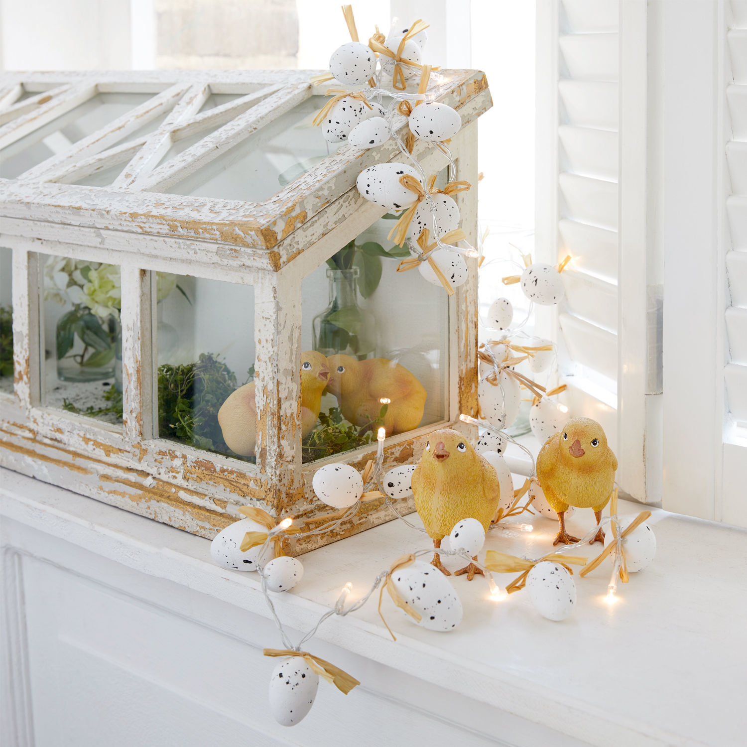 Guirlande décorative d'œufs blancs avec nœuds et poussins jaunes sur rebord de fenêtre blanc