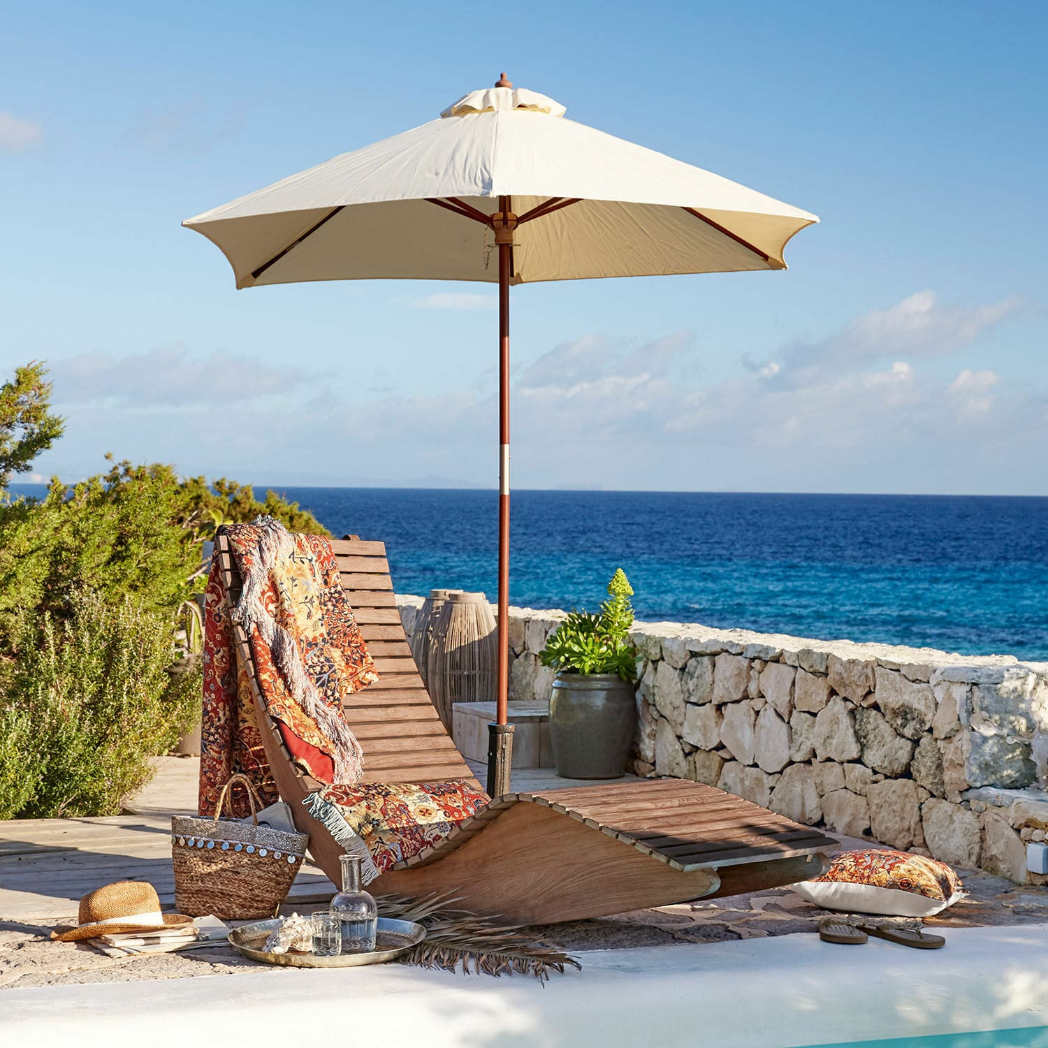 Chaise longue à bascule Wenham Chaise longue en bois avec parasol crème et plaid coloré au bord de la piscine face à la mer