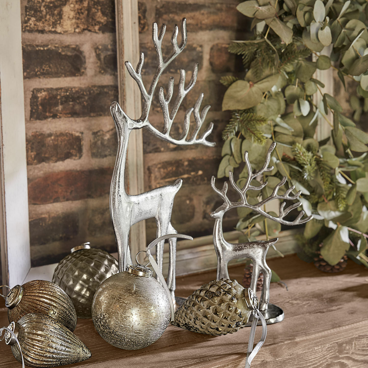 Lot de 2 rennes décoratifs Zerlay Figurines de rennes argentées et décorations de Noël posées sur une table en bois avec feuillage vert