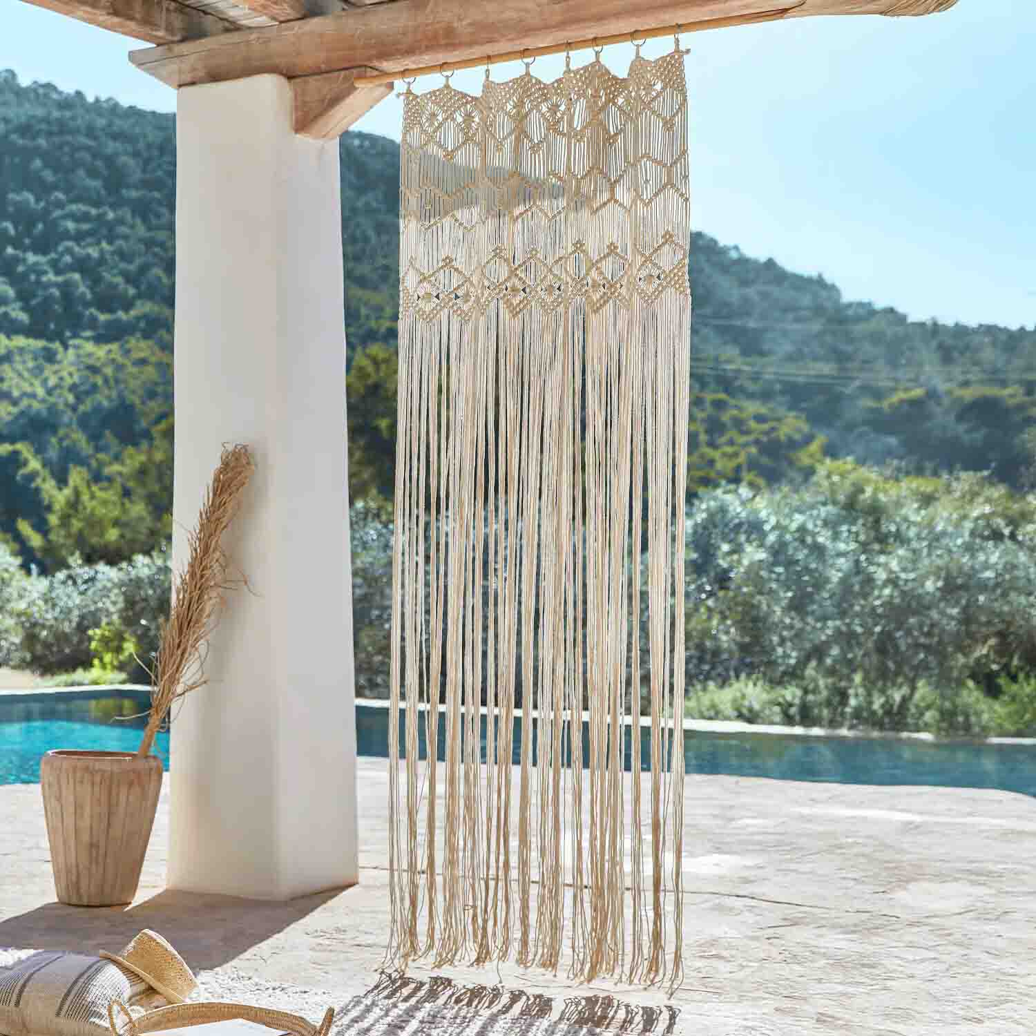 Beige katoenen macramé hangend aan houten balk, boho decoratie op terras met zwembadzicht