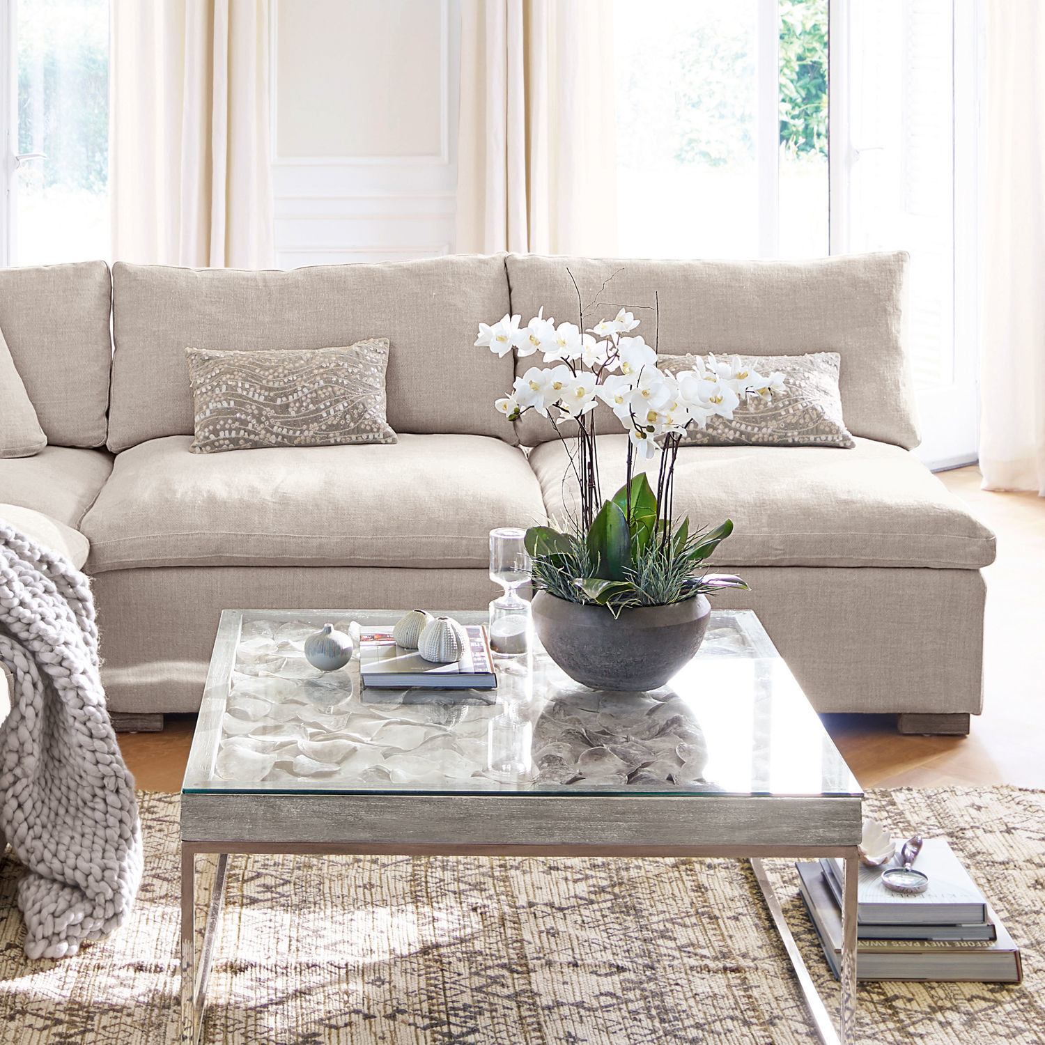 Fauteuil Bennington Canapé beige en tissu avec coussins décoratifs et table basse en verre avec plante blanche