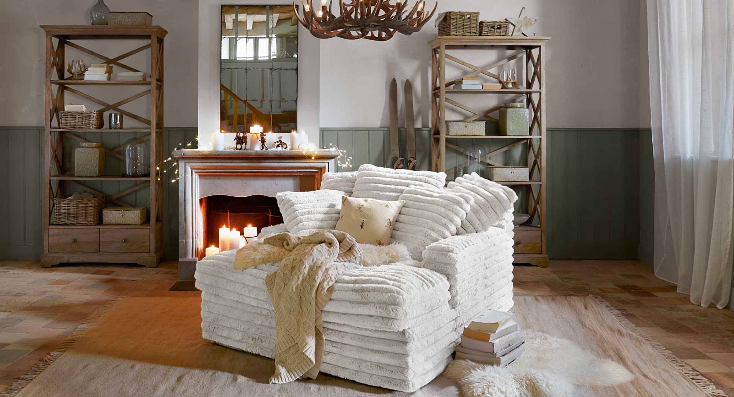 Fauteuil blanc en tissu doux style chalet dans un salon avec cheminée et étagères en bois rustique