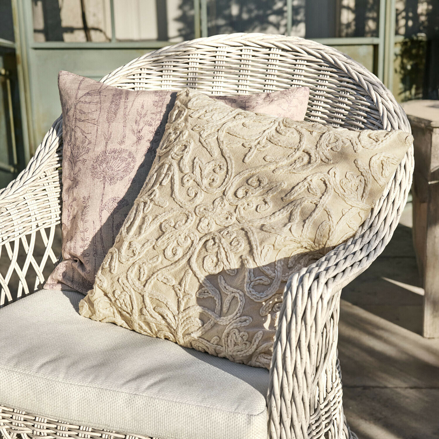 Kussenhoes set van 2 Floraine Twee decoratieve kussens in beige en roze op een witte rotan stoel op een zonnig terras