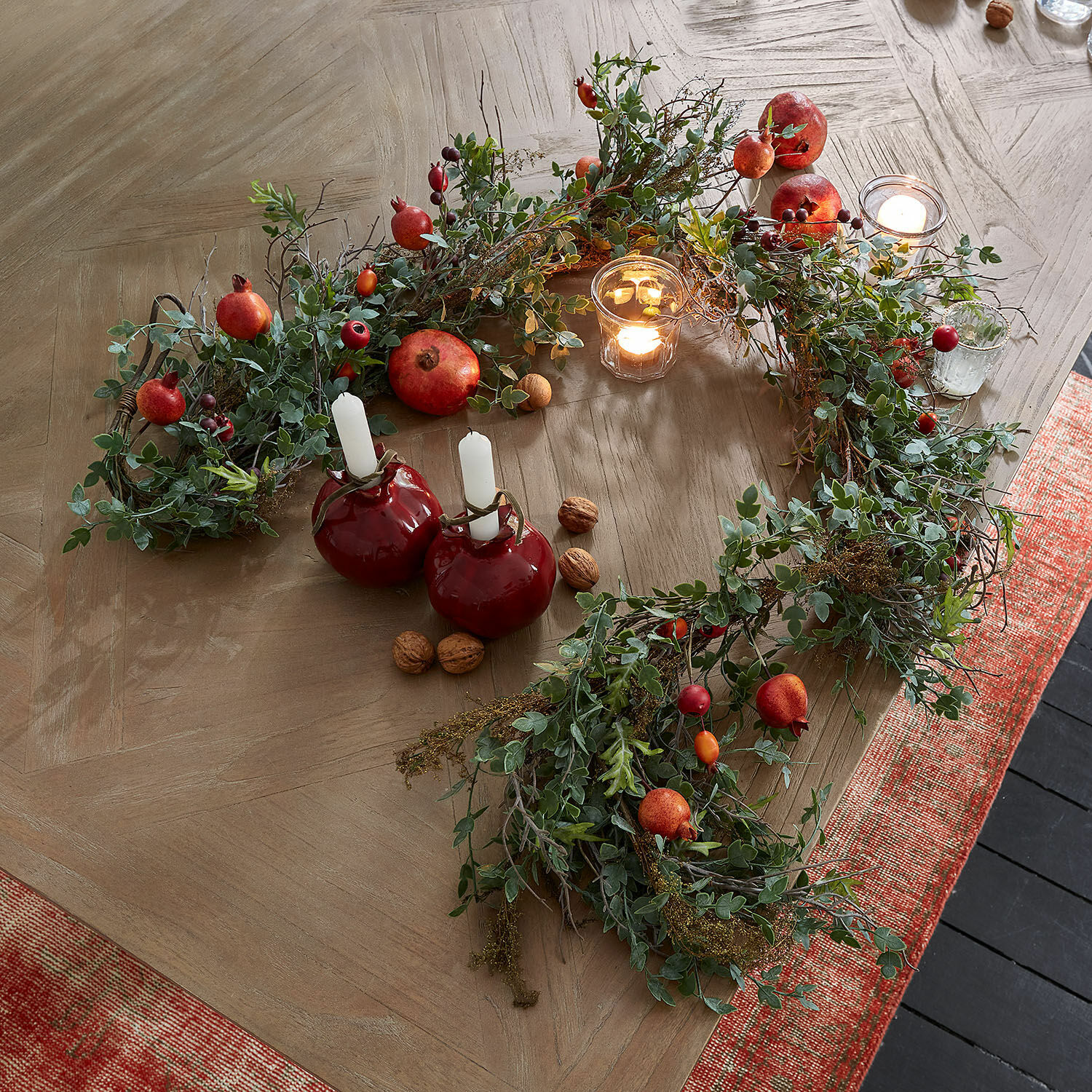 Guirlande Karidah Couronne décorative en feuillage vert et fruits rouges sur table en bois avec bougies allumées