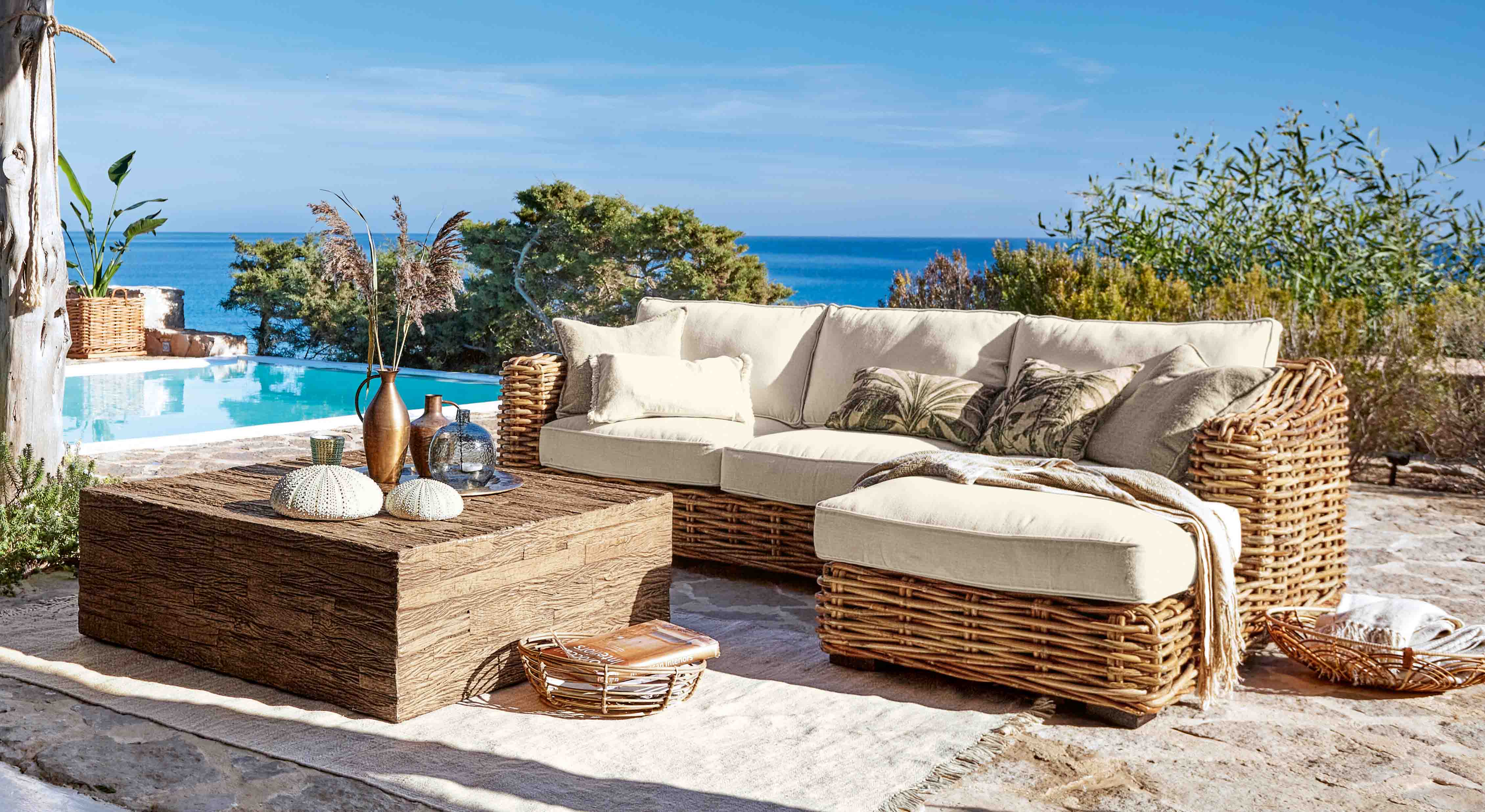 Ensemble de mobilier d'extérieur en rotin avec coussins crème près d'une piscine avec vue sur la mer