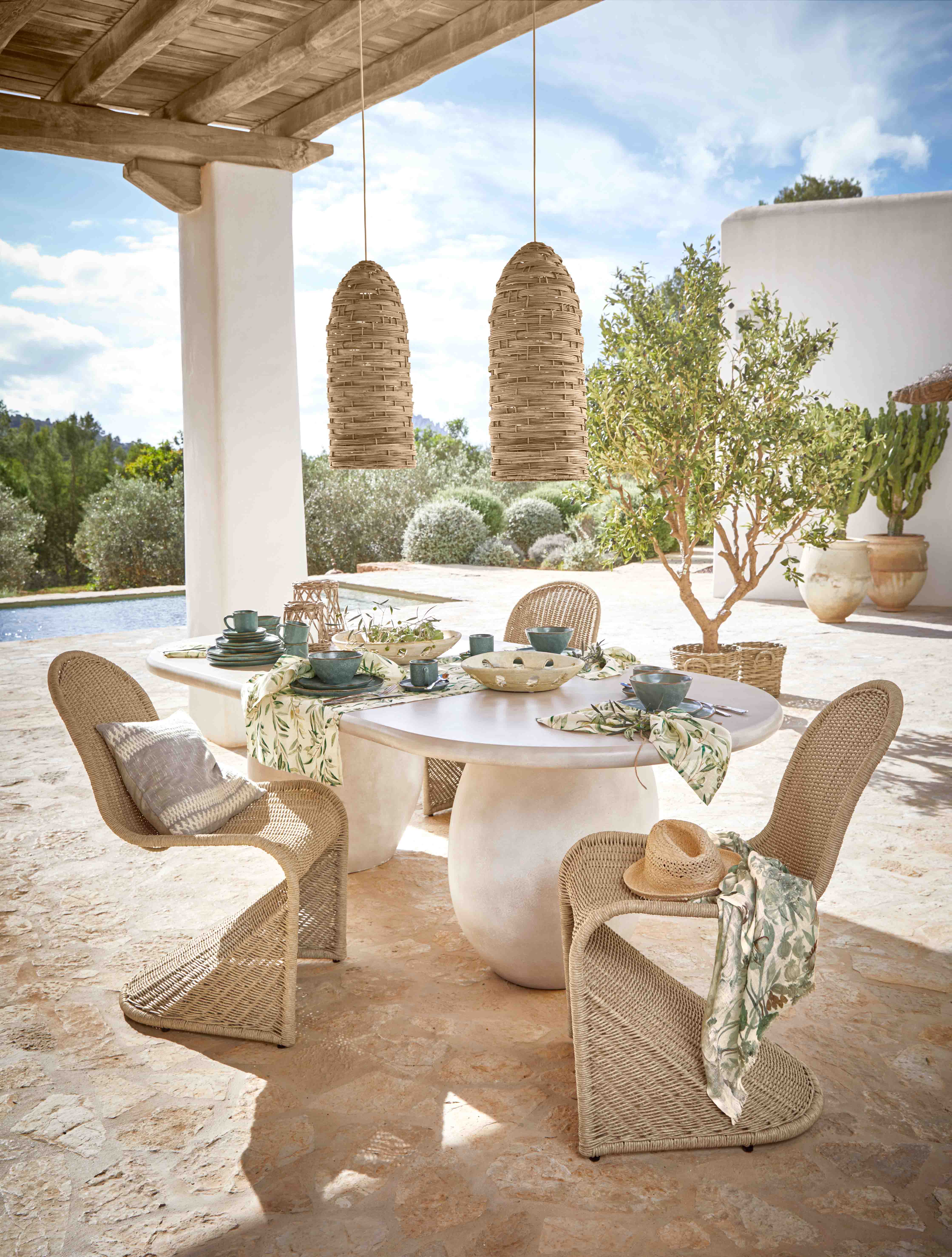 Tuinmeubelset met gevlochten stoelen en witte tafel op terras met tafeldecoratie