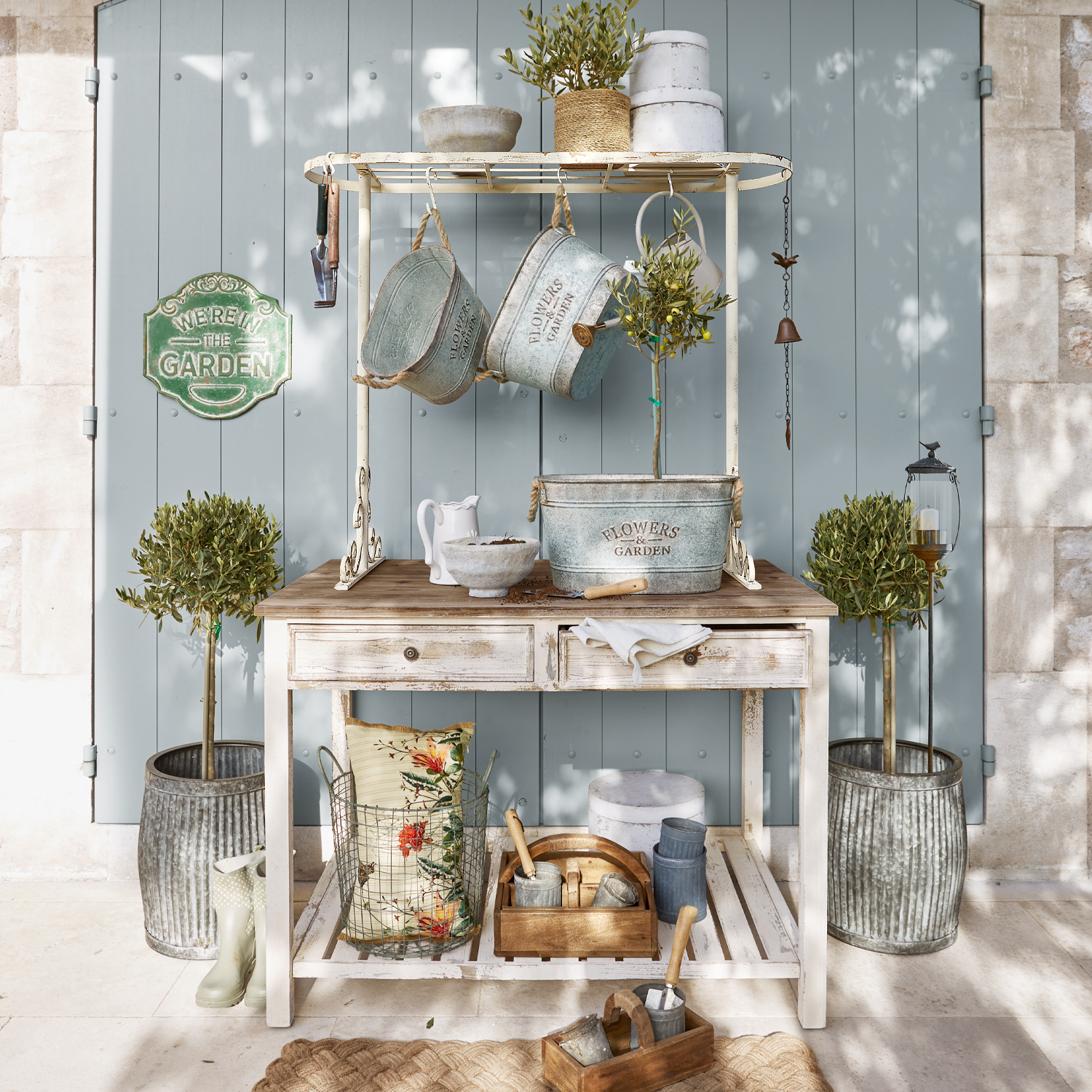 Witte houten tuintafel met metalen bloempotten en tuingereedschap voor een blauwe deur