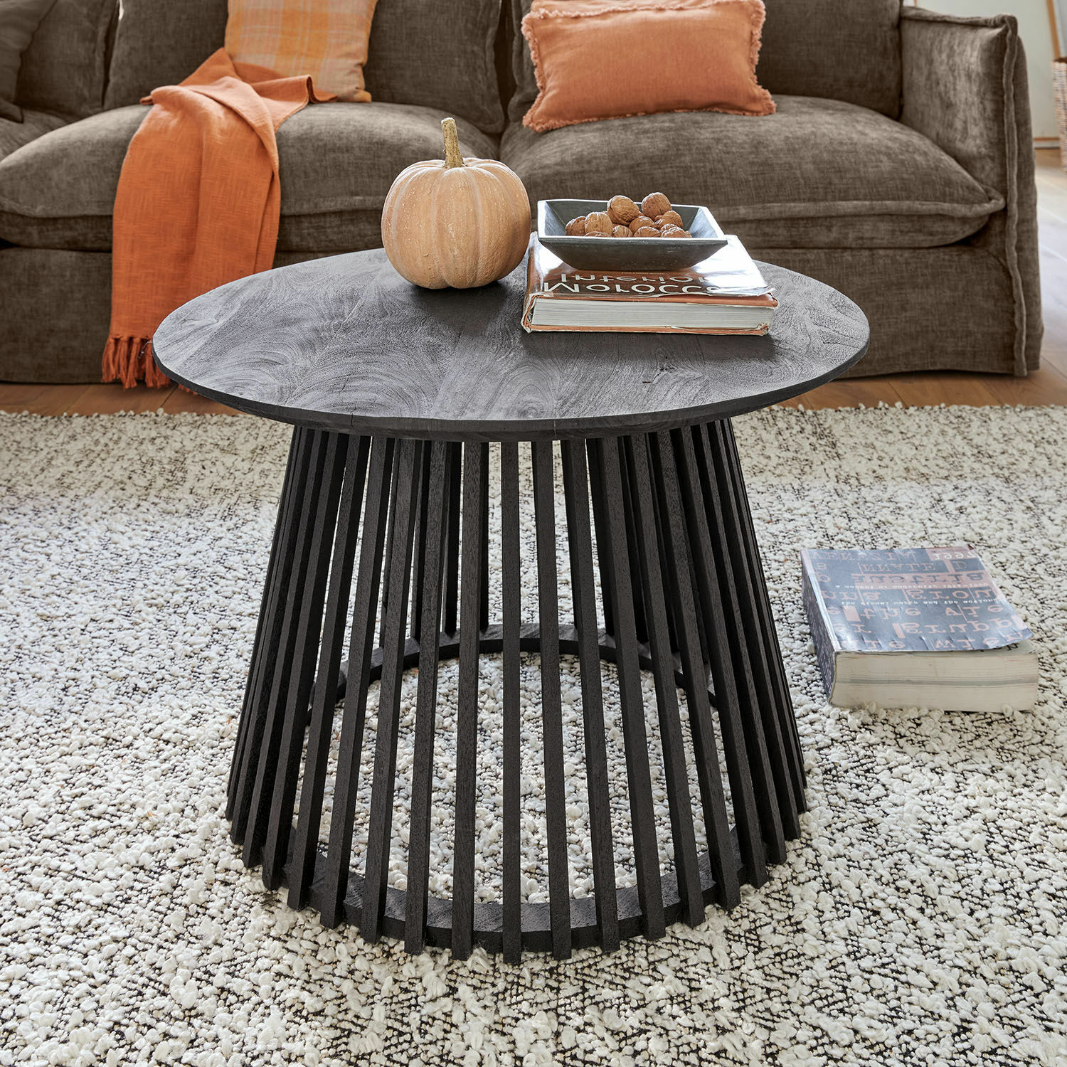 Table basse Montaril Table basse ronde noire en bois de manguier avec base ajourée sur tapis clair dans un salon