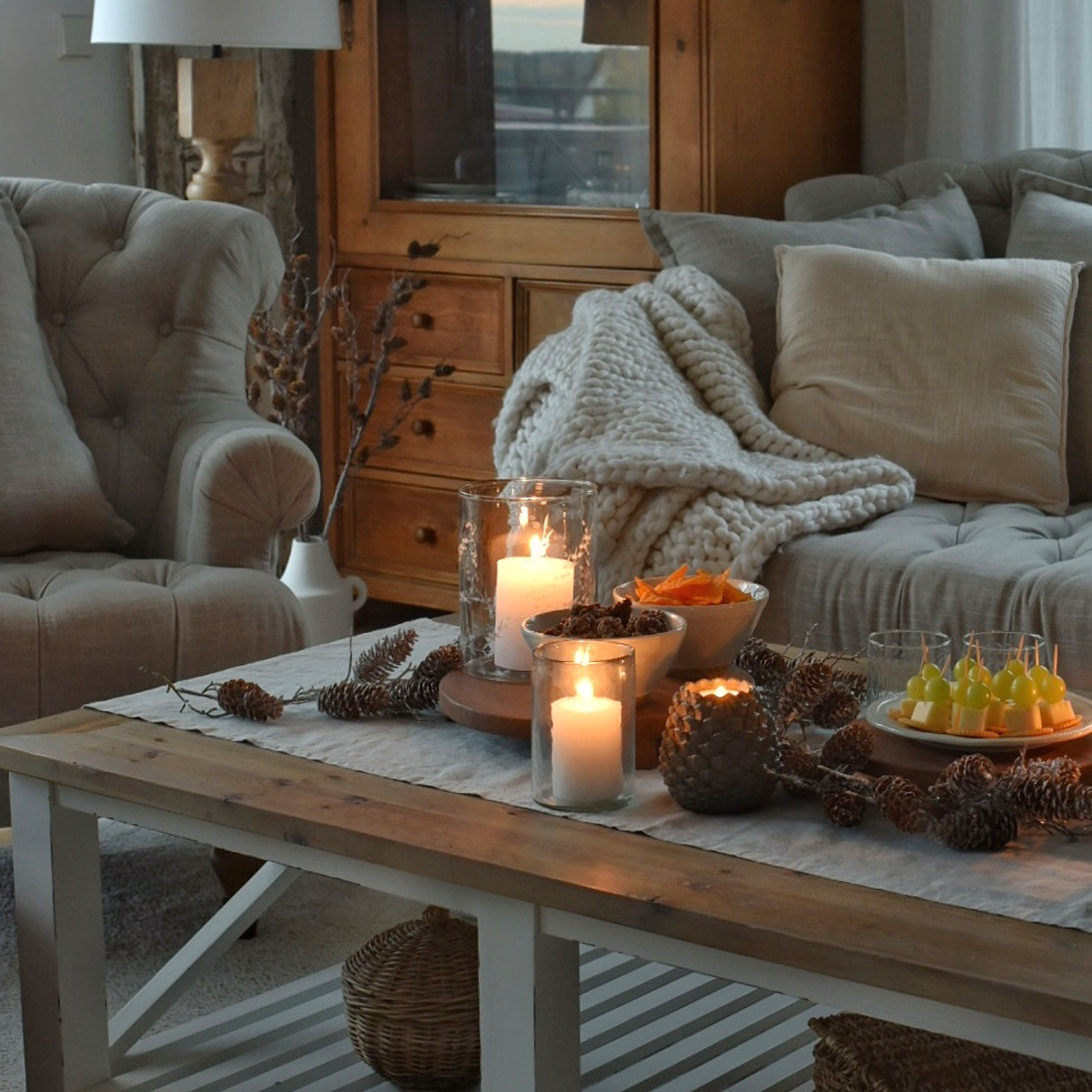 Salon chaleureux avec table en bois, bougies allumées et plaid gris sur canapé moelleux