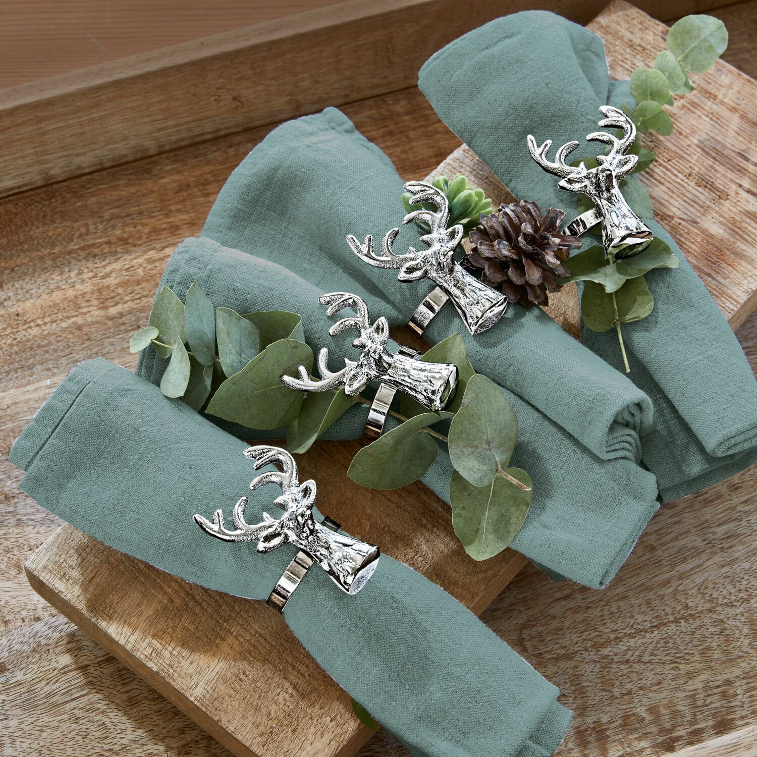 Ensemble de quatre serviettes en lin vert avec anneaux en métal tête de cerf sur plateau en bois
